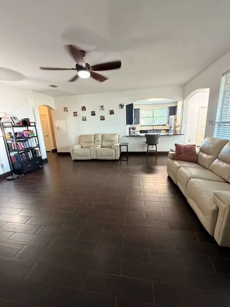 Spacious living area featuring dark wood-look tile flooring, an integrated ceiling fan with lighting, and arched doorways