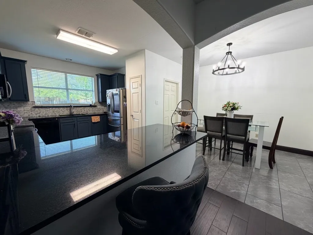 Kitchen featuring dark cabinetry, dark countertops, a tile backsplash, and a stainless steel refrigerator