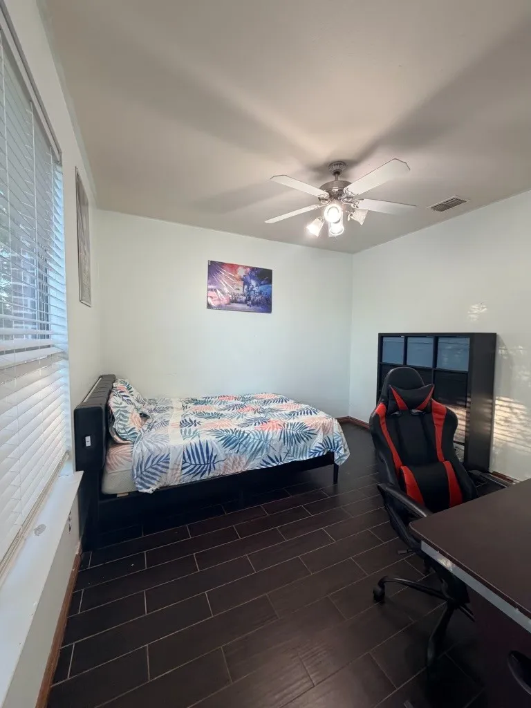 Spacious room featuring dark wood-finish flooring, a ceiling fan with integrated lighting, and multiple windows with blinds