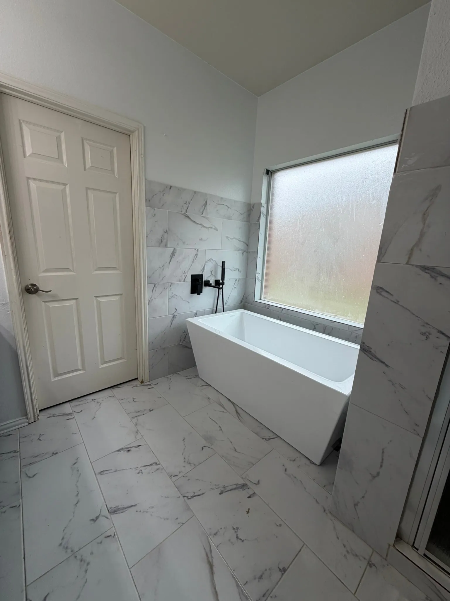 Freestanding soaking tub with matte black fixtures, set against large format wall tile