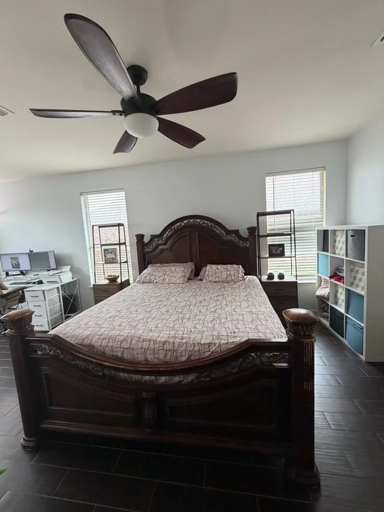 Spacious room featuring dark wood-finish flooring, two large windows with blinds, and white painted walls