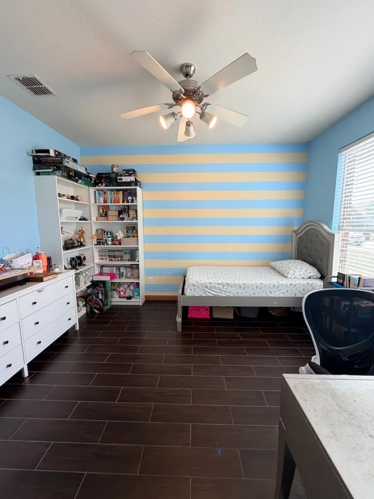Spacious room featuring wood-finish flooring, a ceiling fan with integrated lighting, and a window with blinds