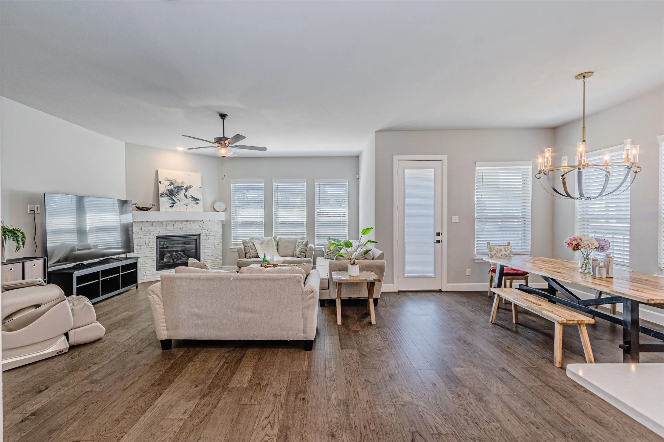Open-concept living and dining area with wood-finish flooring, a white brick fireplace, and a contemporary chandelier