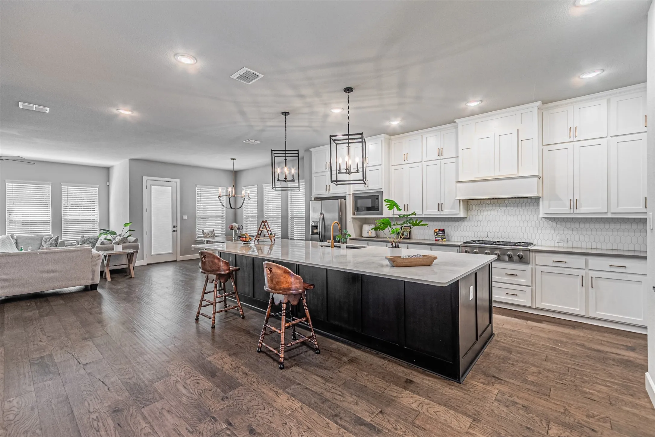 Open-concept kitchen with a large island, white shaker cabinetry, stainless steel appliances, and wood-finish flooring