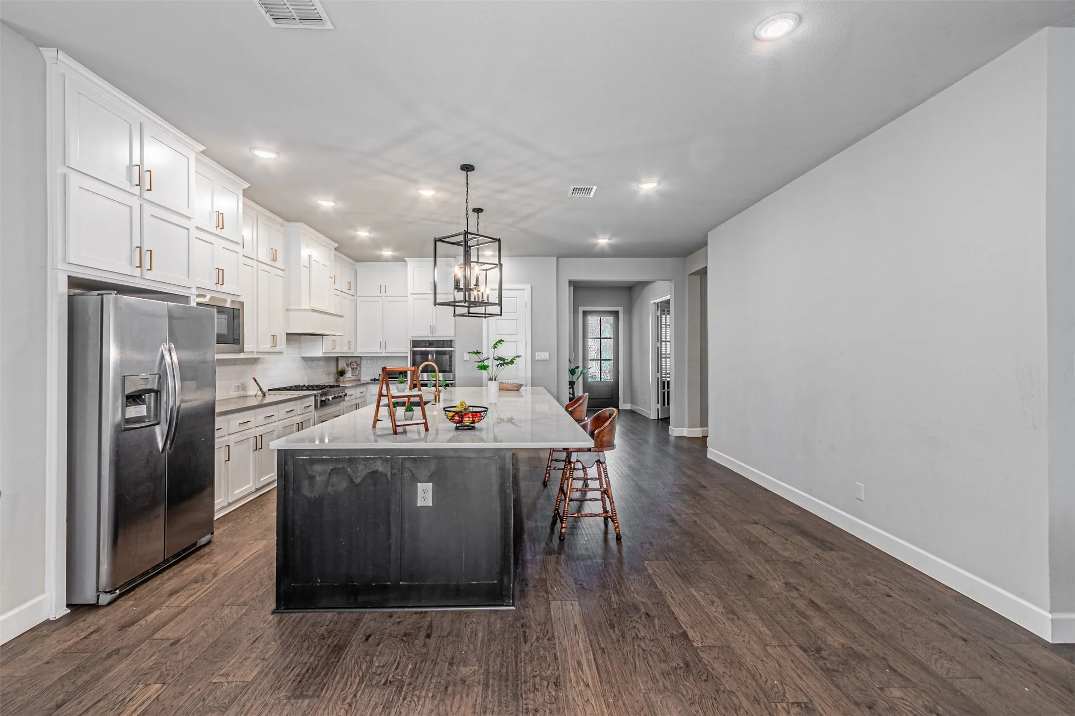 Kitchen featuring a large island with a light-toned countertop, white cabinetry with gold-toned hardware, stainless steel appliances, and dark wood-finish flooring
