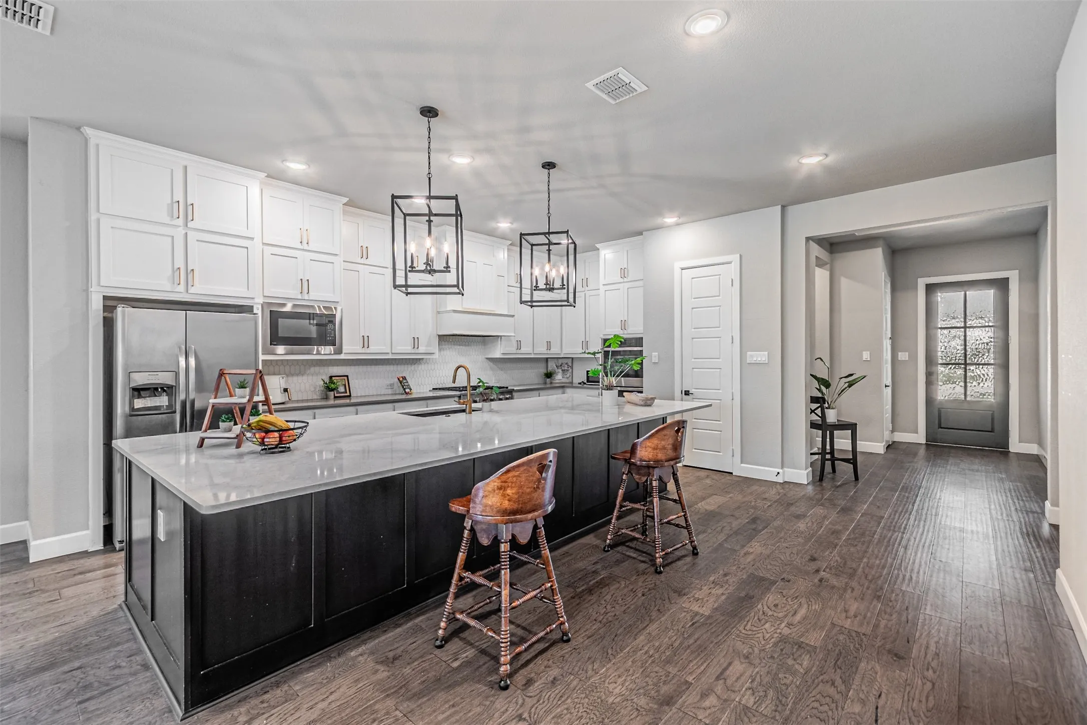 Gourmet kitchen featuring a large central island, white cabinetry, stainless steel appliances, and dark wood-finish flooring
