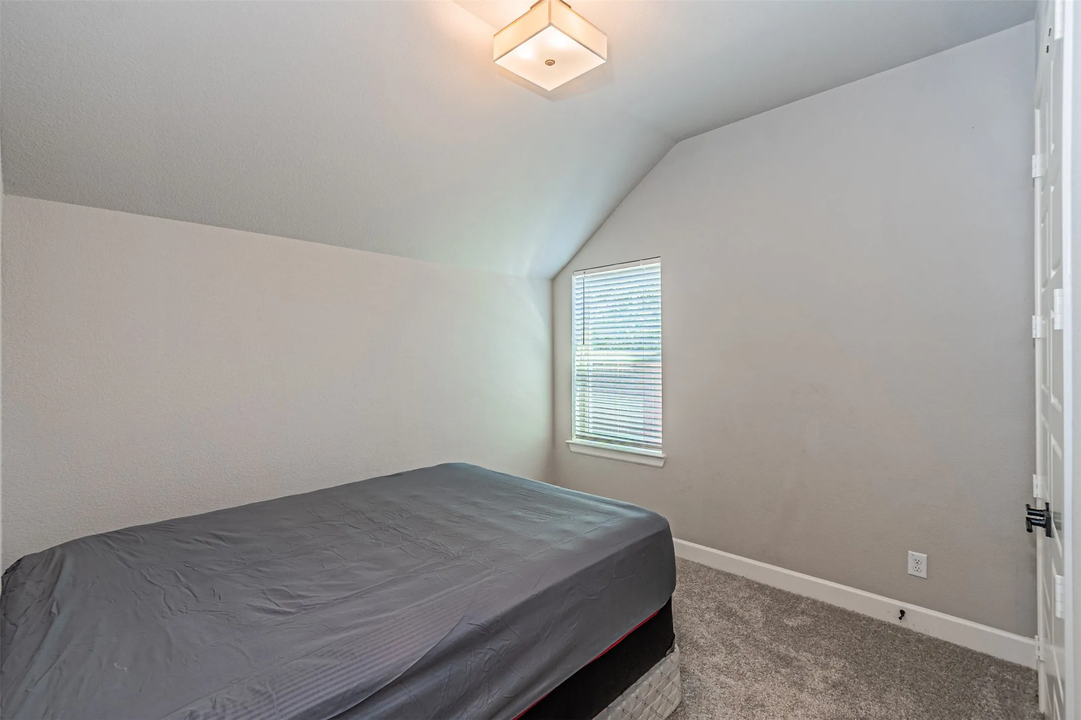 Vaulted ceilings featuring a flush mount light fixture, textured carpet flooring, and a window with blinds