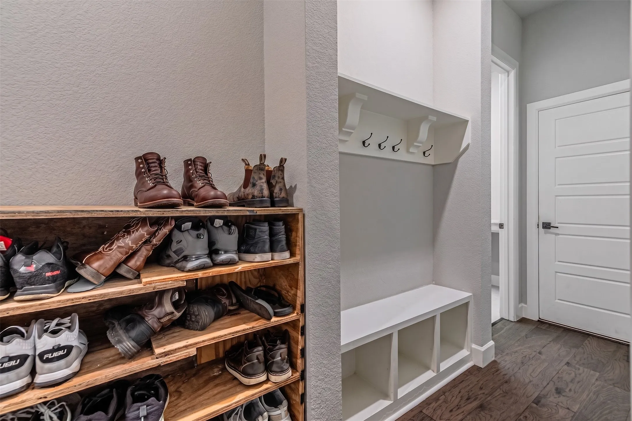 Built-in mudroom features a white bench with cubby storage, upper shelf with coat hooks, and durable wood-finish flooring
