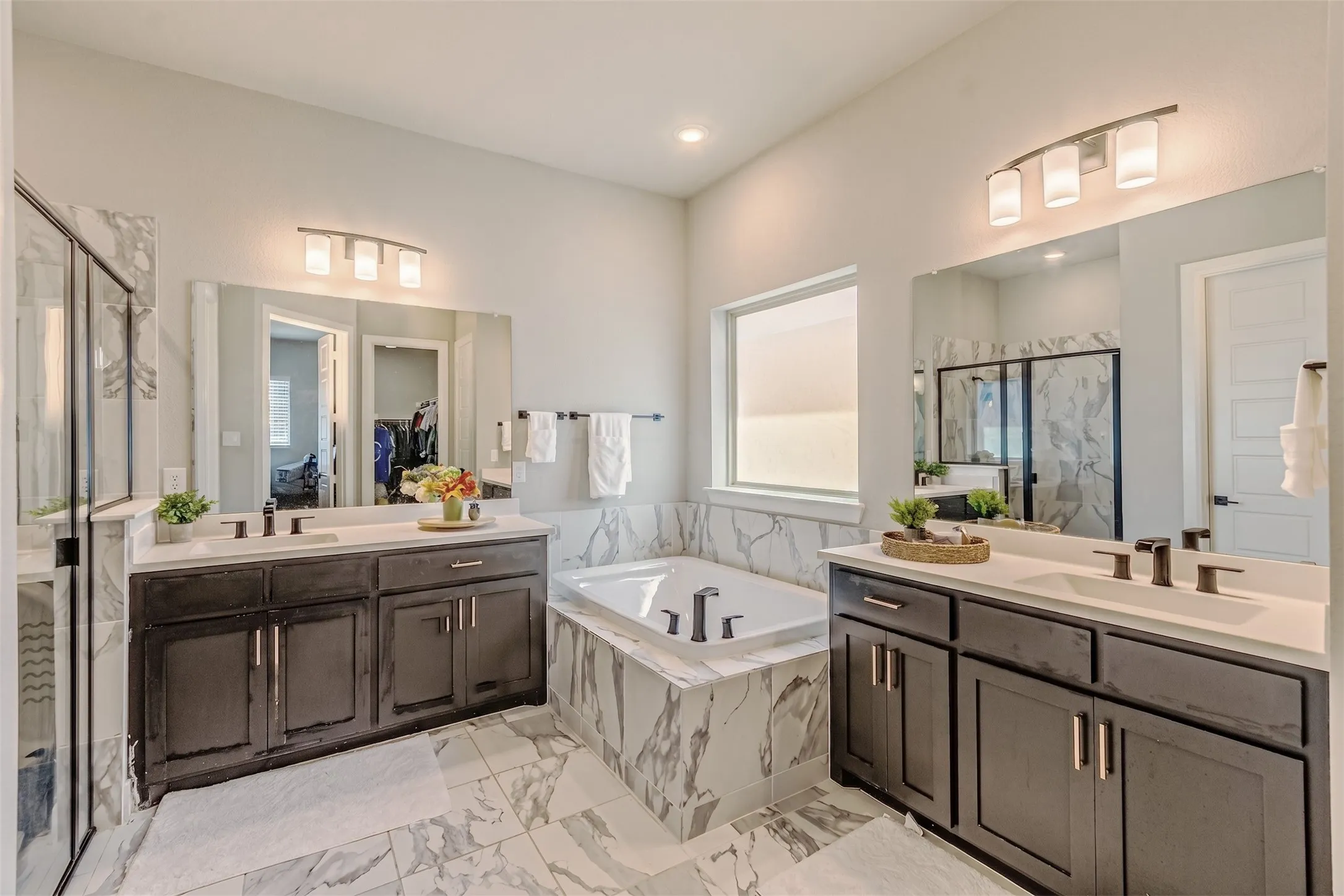 Dual vanities with undermount sinks and dark cabinetry, white countertops, tile flooring, built-in tub with tile surround, and a glass-enclosed shower