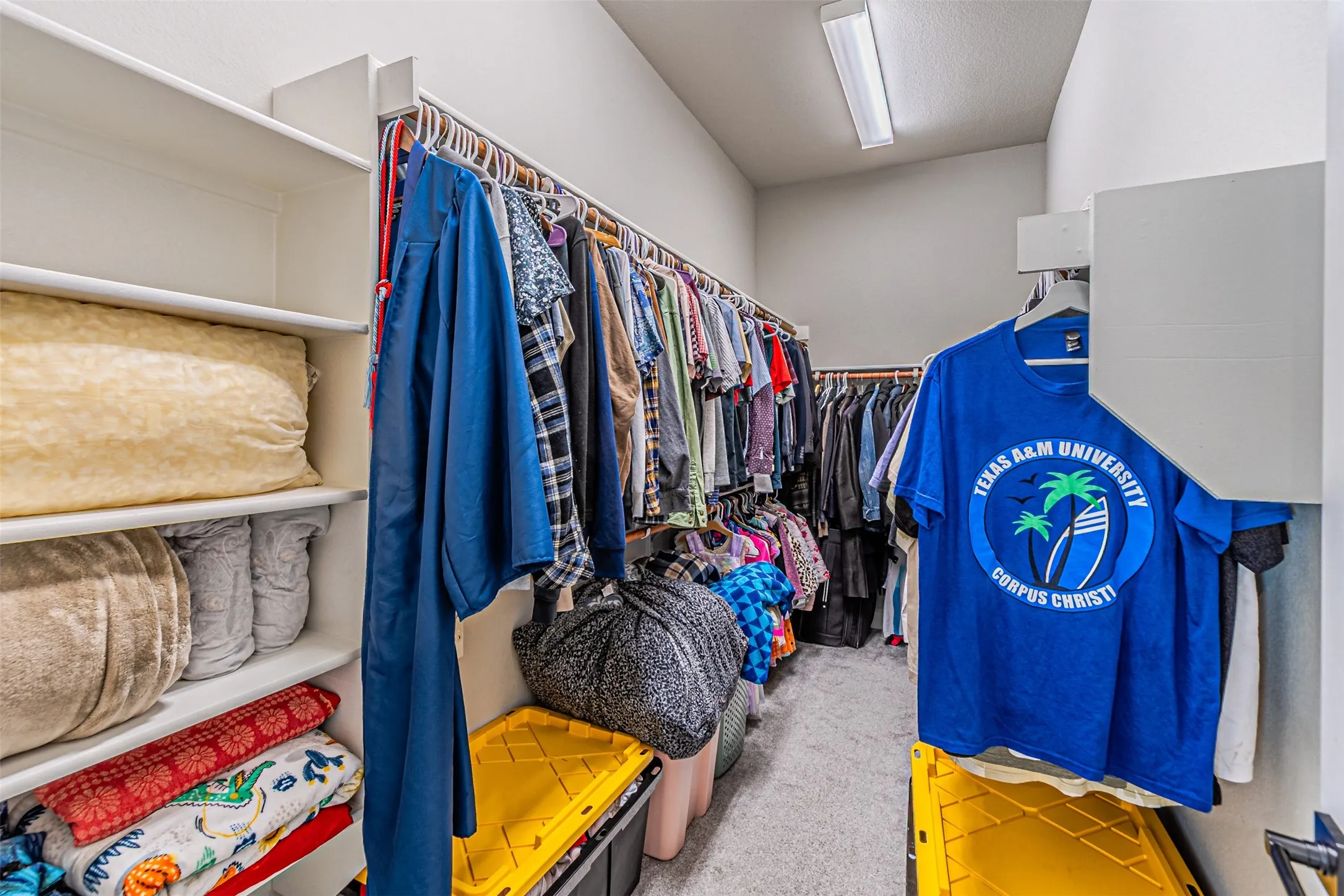 Walk-in closet featuring white shelving, multiple clothing rods, and overhead lighting