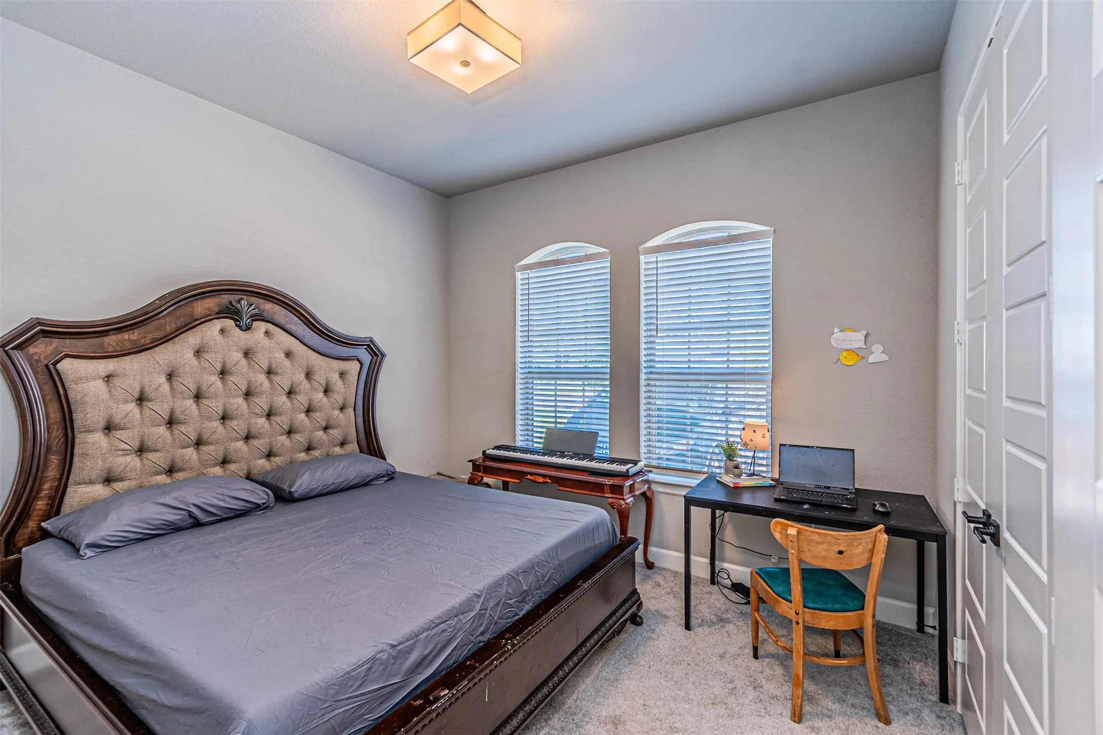 Arched windows with blinds, light gray wall paint, square ceiling light fixture, and textured carpeting