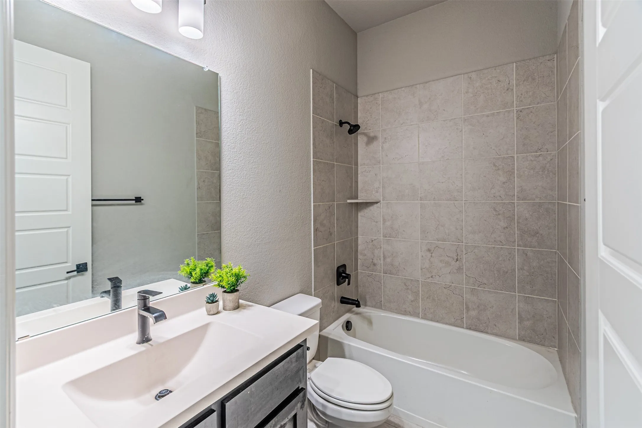 Bathroom featuring a built-in tub with tile surround, black-finish plumbing fixtures, a floating vanity with integrated sink, and an overhead vanity light