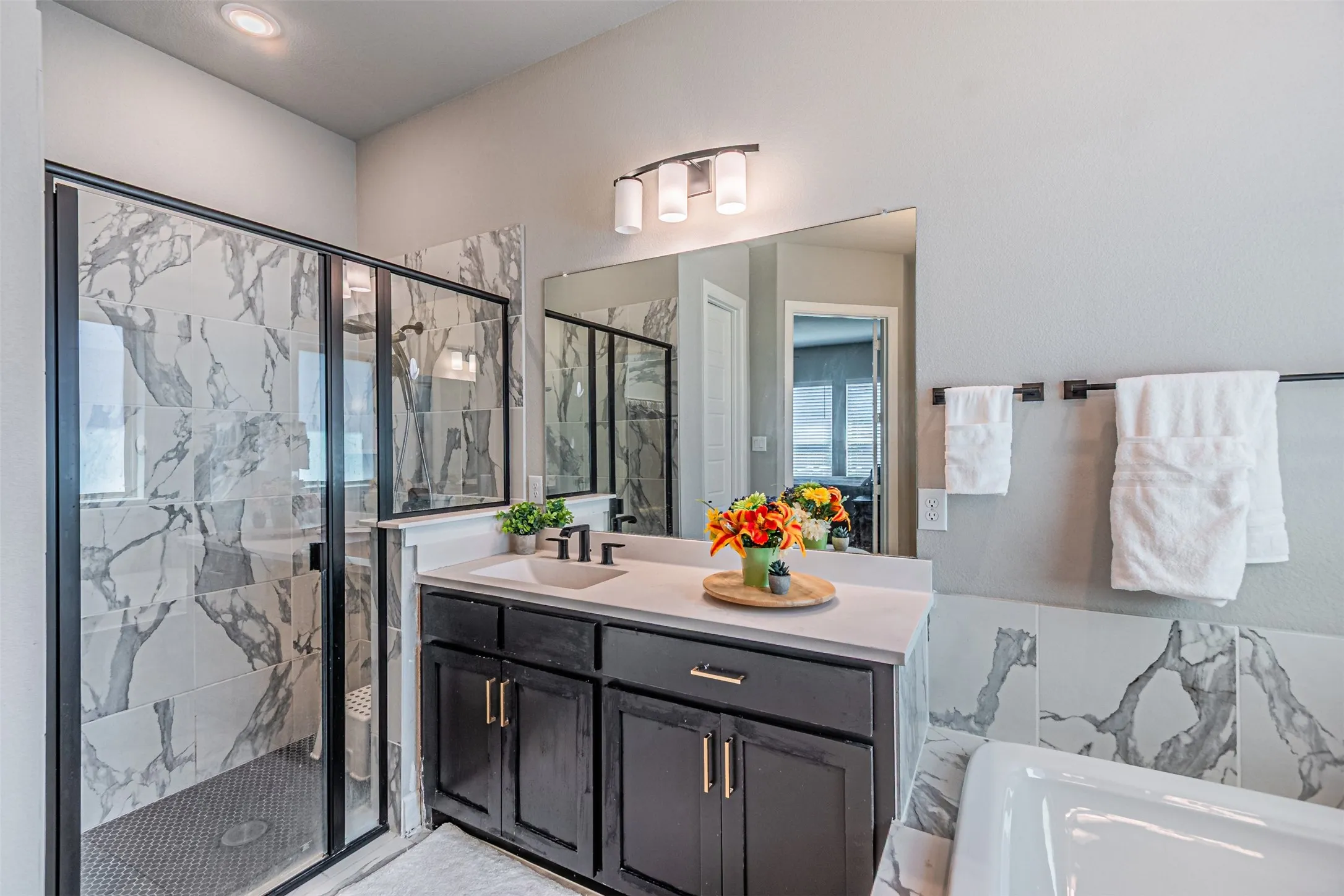 Spacious bathroom featuring a glass-enclosed shower with tiled walls and a dark tile floor, a single vanity with a light-toned countertop, and a built-in bathtub with tiled surround
