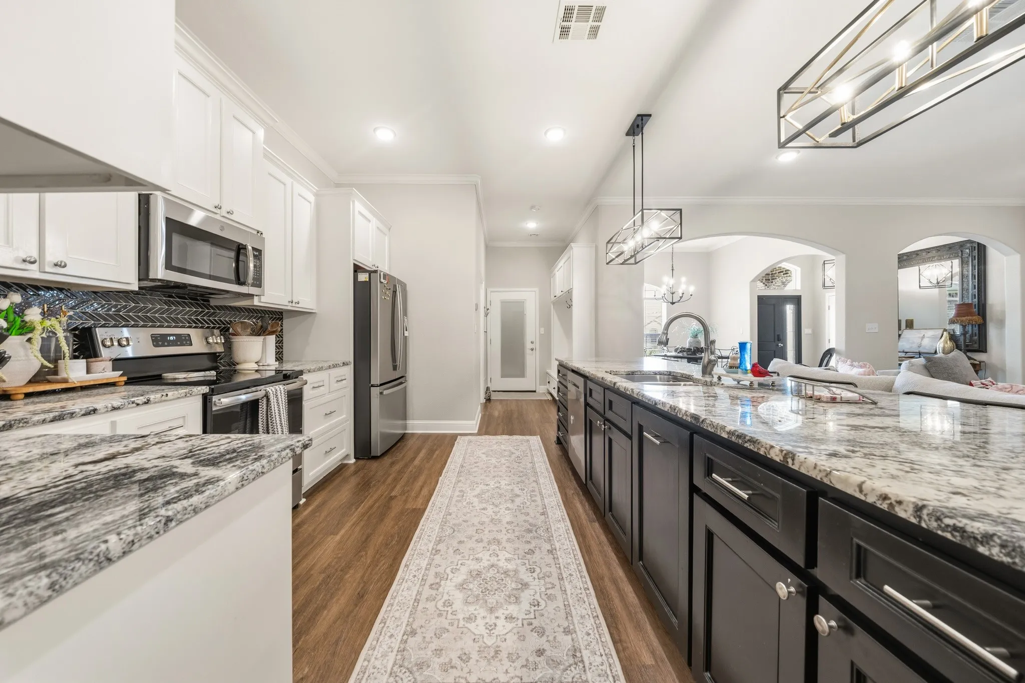 Kitchen featuring an expansive island with a light-toned countertop, stainless steel appliances, white upper cabinetry, dark lower cabinetry, and wood-finish​​‌​​​​‌​​‌‌​‌‌​​​‌‌​‌​‌​‌​​​‌​​ flooring