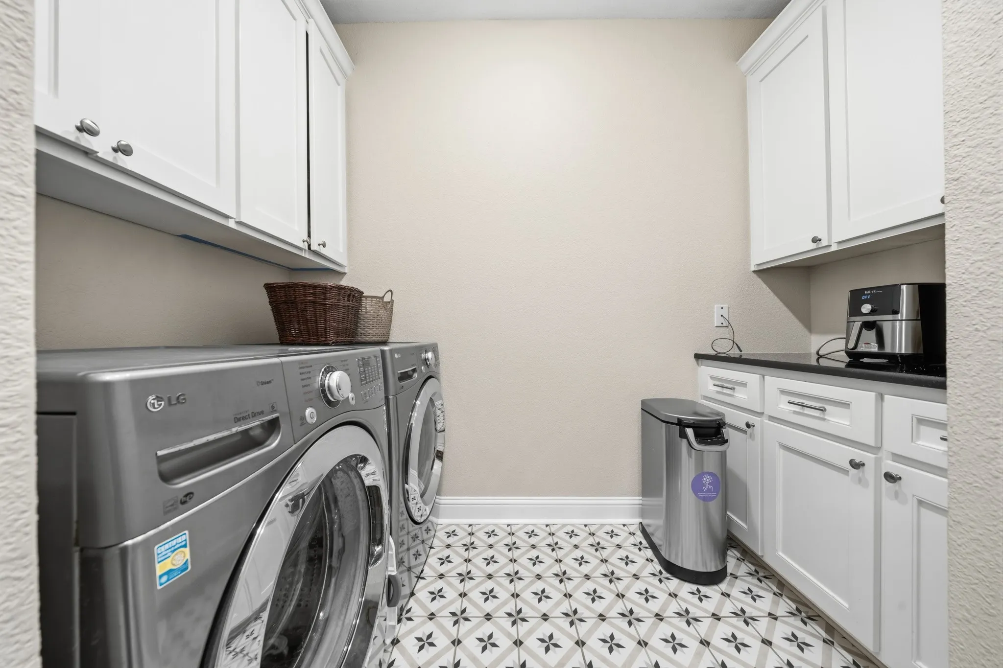 Laundry room featuring patterned floor tile, white shaker-style cabinetry, and dark countertops
