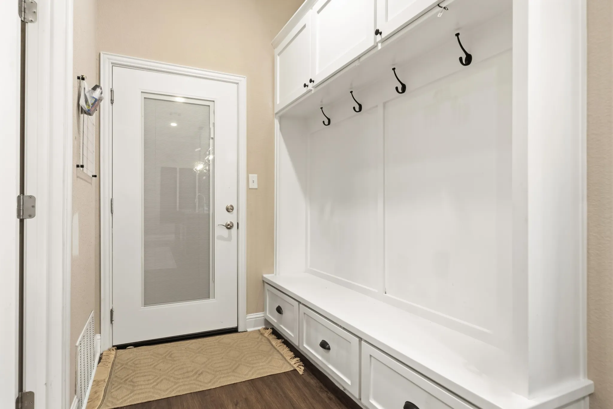 Built-in white cabinetry with a bench and storage drawers, featuring black hooks and hardware