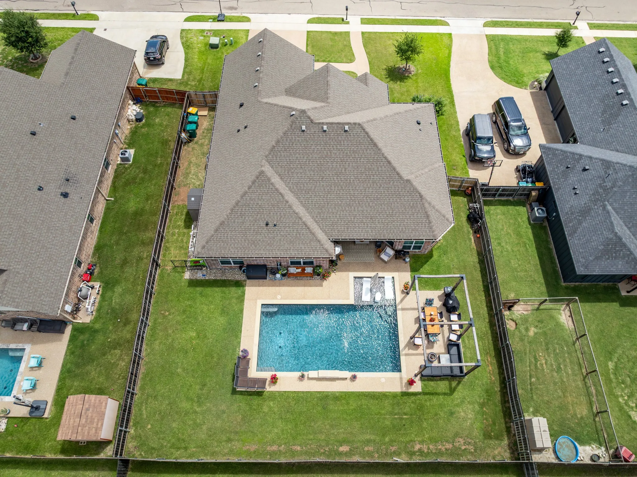 Spacious fenced backyard featuring a rectangular swimming pool with surrounding patio, a covered outdoor living area, and expansive green lawn