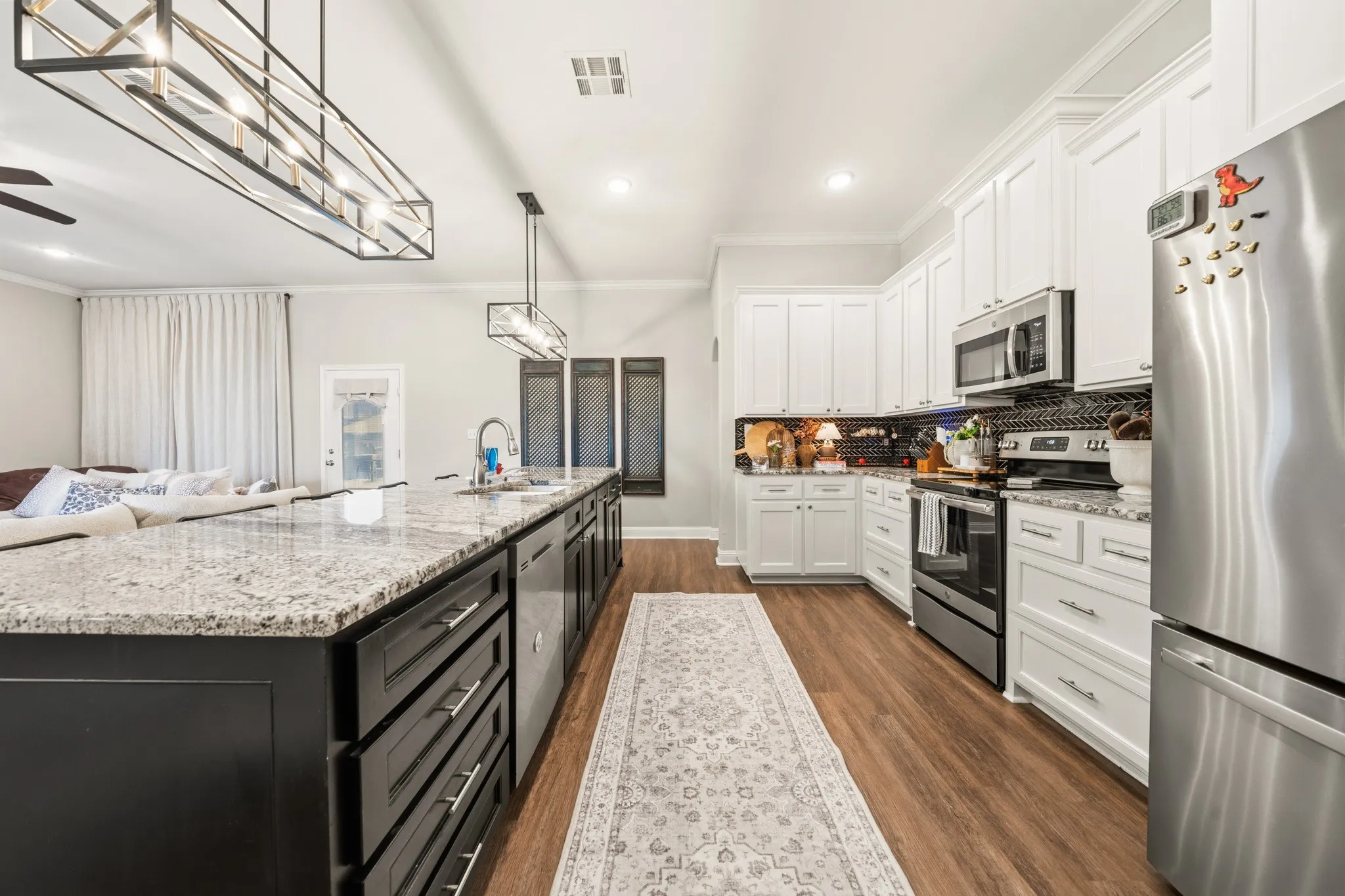 Modern kitchen featuring a large island with stone countertop, white shaker cabinetry, stainless steel appliances, and wood-finish flooring