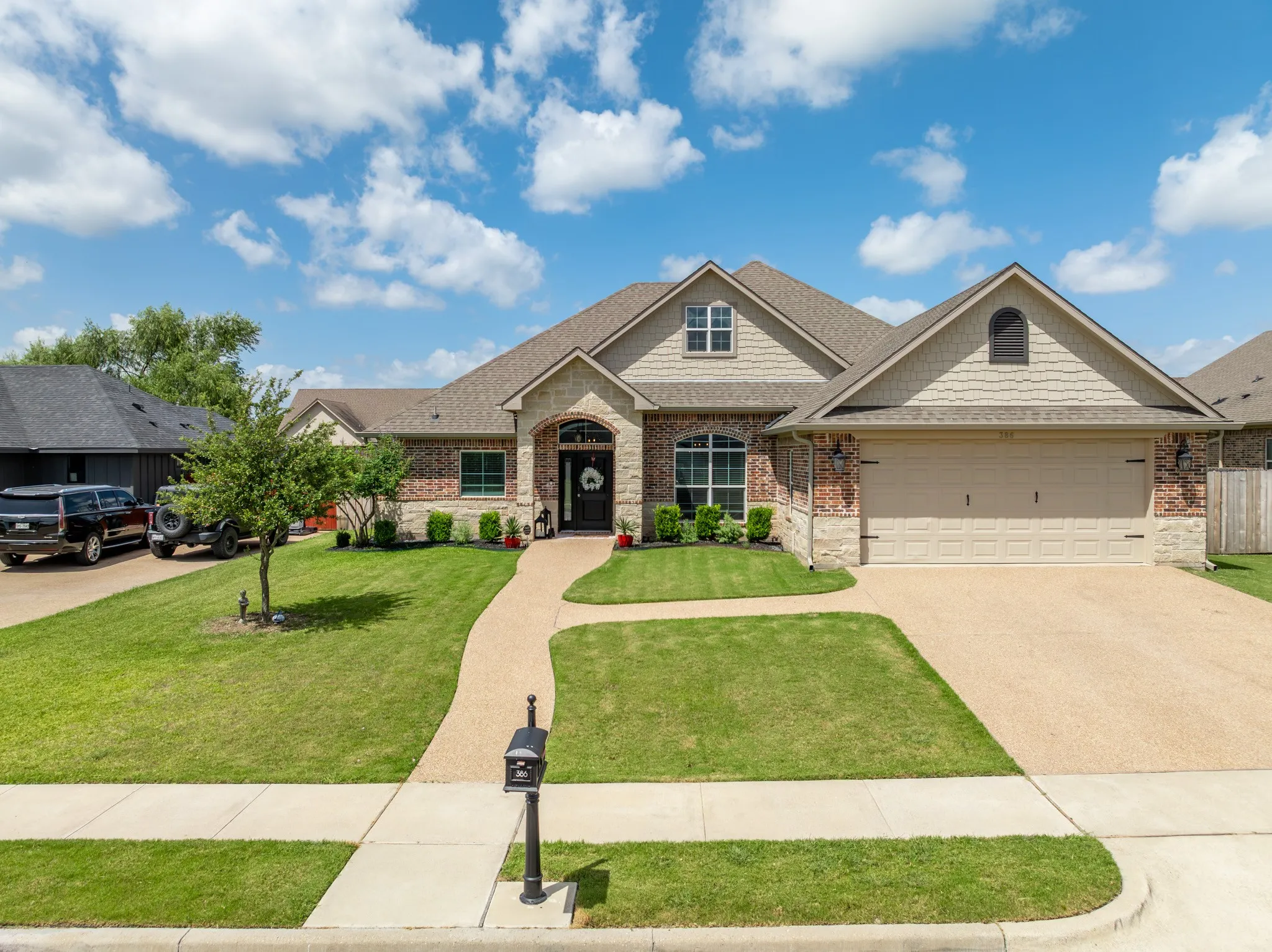 Single-story residence featuring a brick and stone exterior, a gabled roofline, an attached two-car garage, a concrete driveway, and a curved pebble pathway leading to the front entry