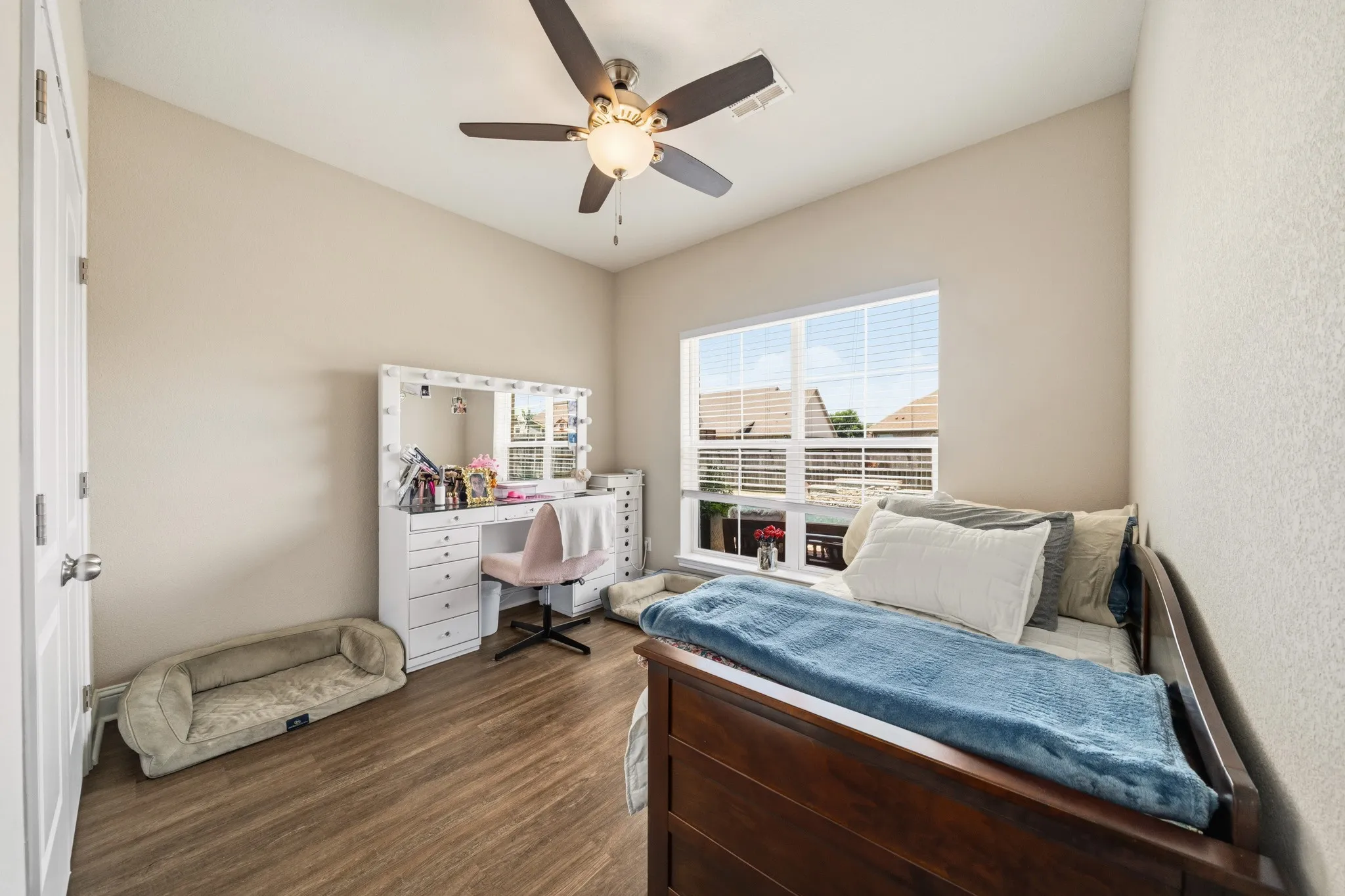Bright interior room featuring wood-finish flooring, a large window with blinds, and a ceiling fan with integrated lighting