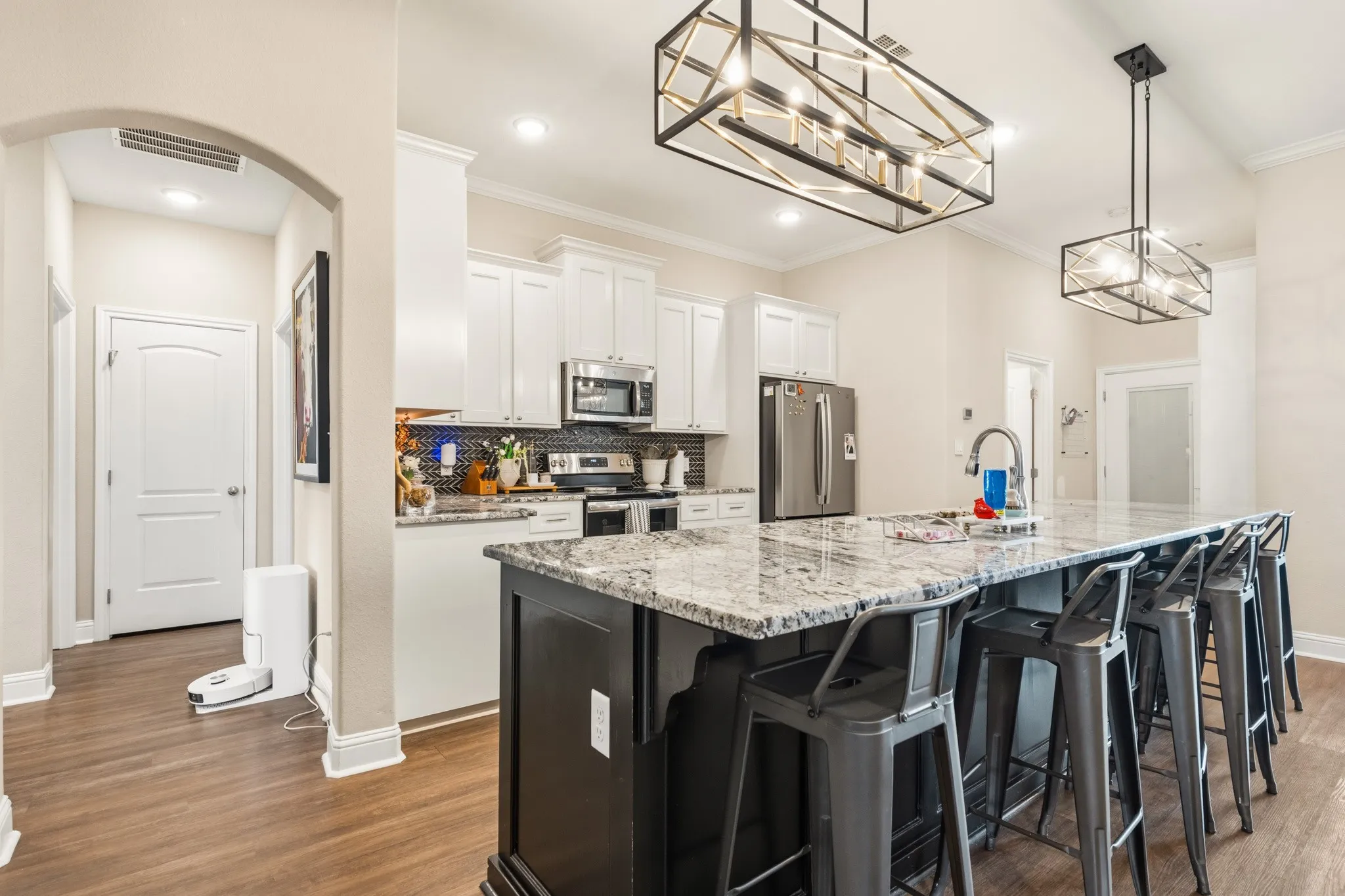 Kitchen featuring a large central island with seating, pendant lighting, stainless steel appliances, white cabinetry, and wood-finish flooring