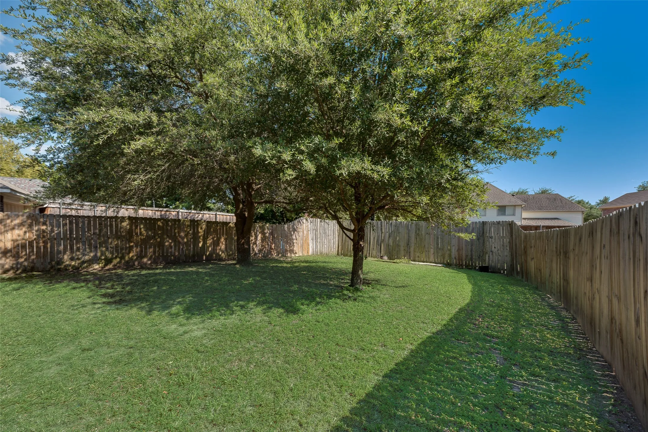 Spacious backyard featuring two mature trees, natural grass, and a wood privacy fence