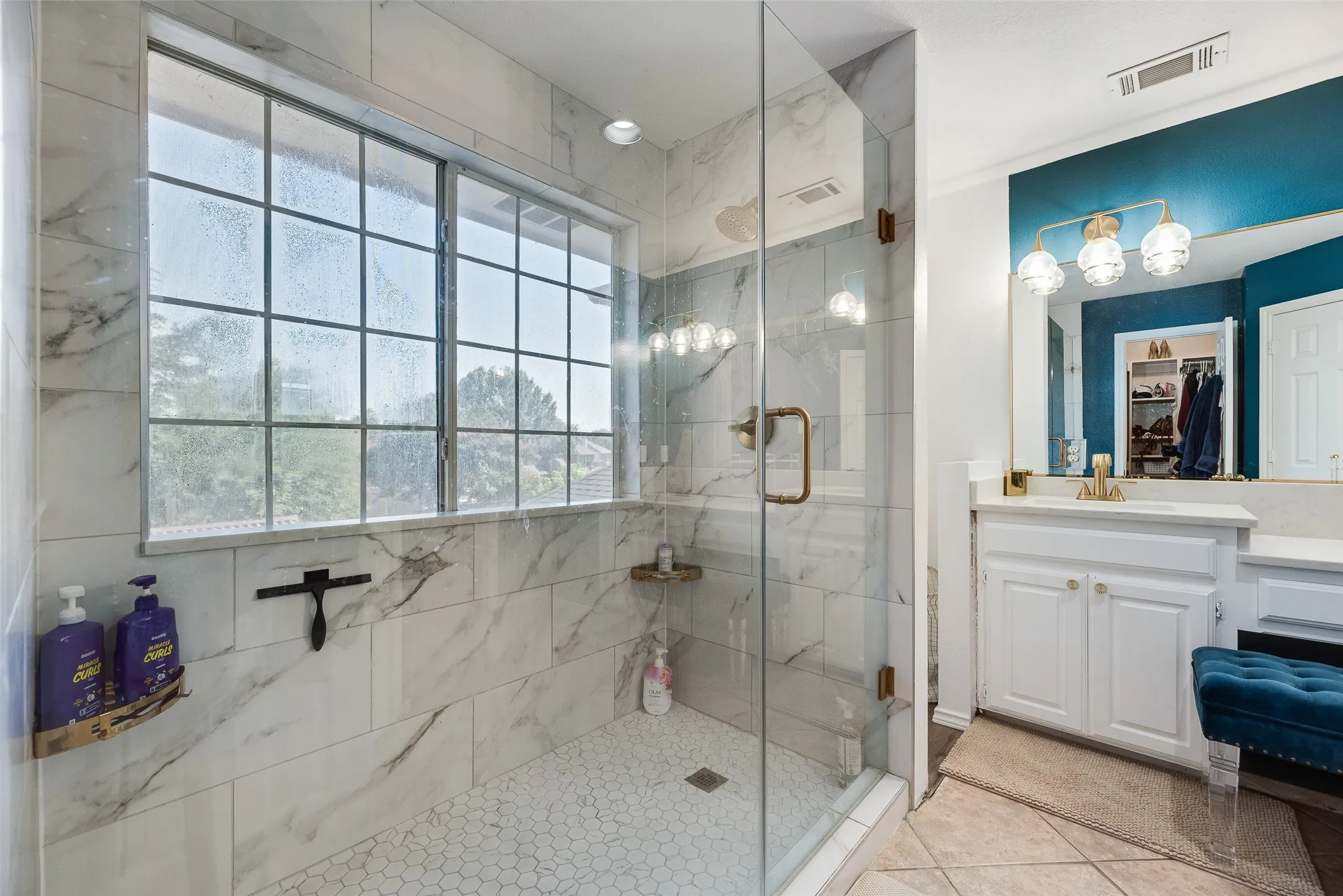 Glass-enclosed shower with large format marble-look tile walls, hexagonal mosaic tile flooring, and an integrated window
