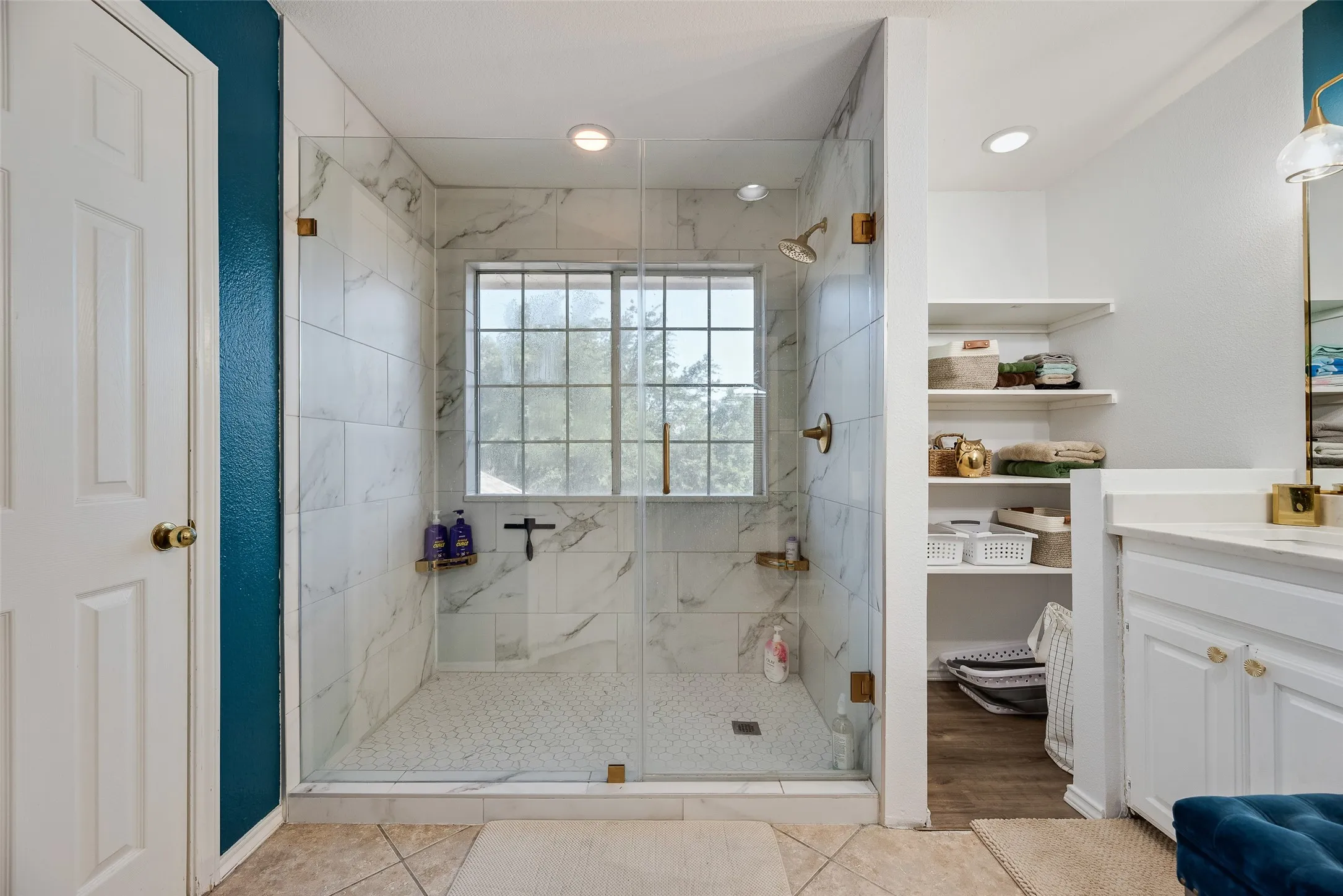 Expansive glass-enclosed shower featuring white marble-look tile, a mosaic tile floor, and a window with grid detailing