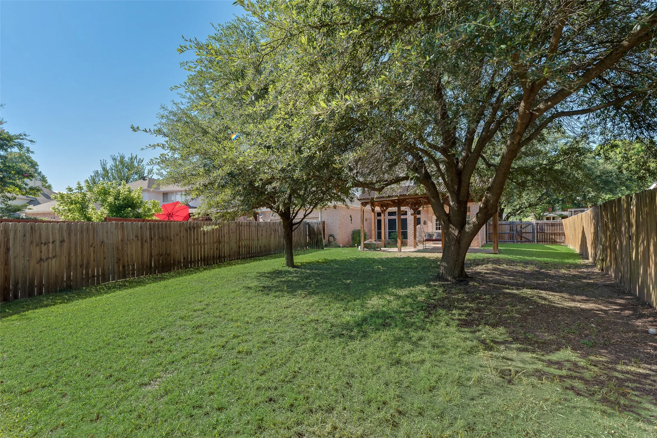 Expansive backyard featuring a manicured lawn, mature trees, and a wooden privacy fence