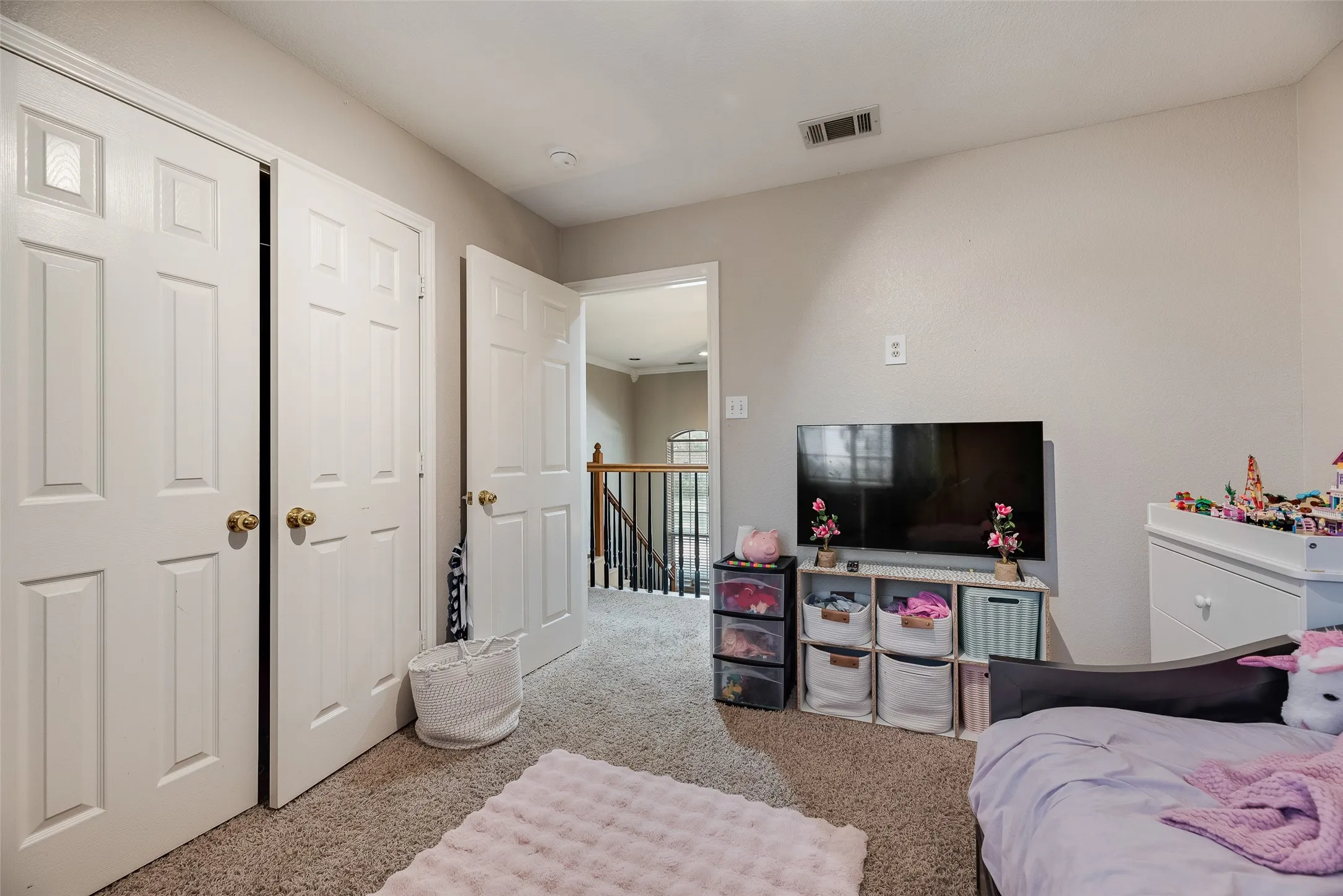Carpeted room with light neutral walls, featuring two paneled doors with brass hardware, and an open doorway leading to a staircase with wood banister and black metal balusters