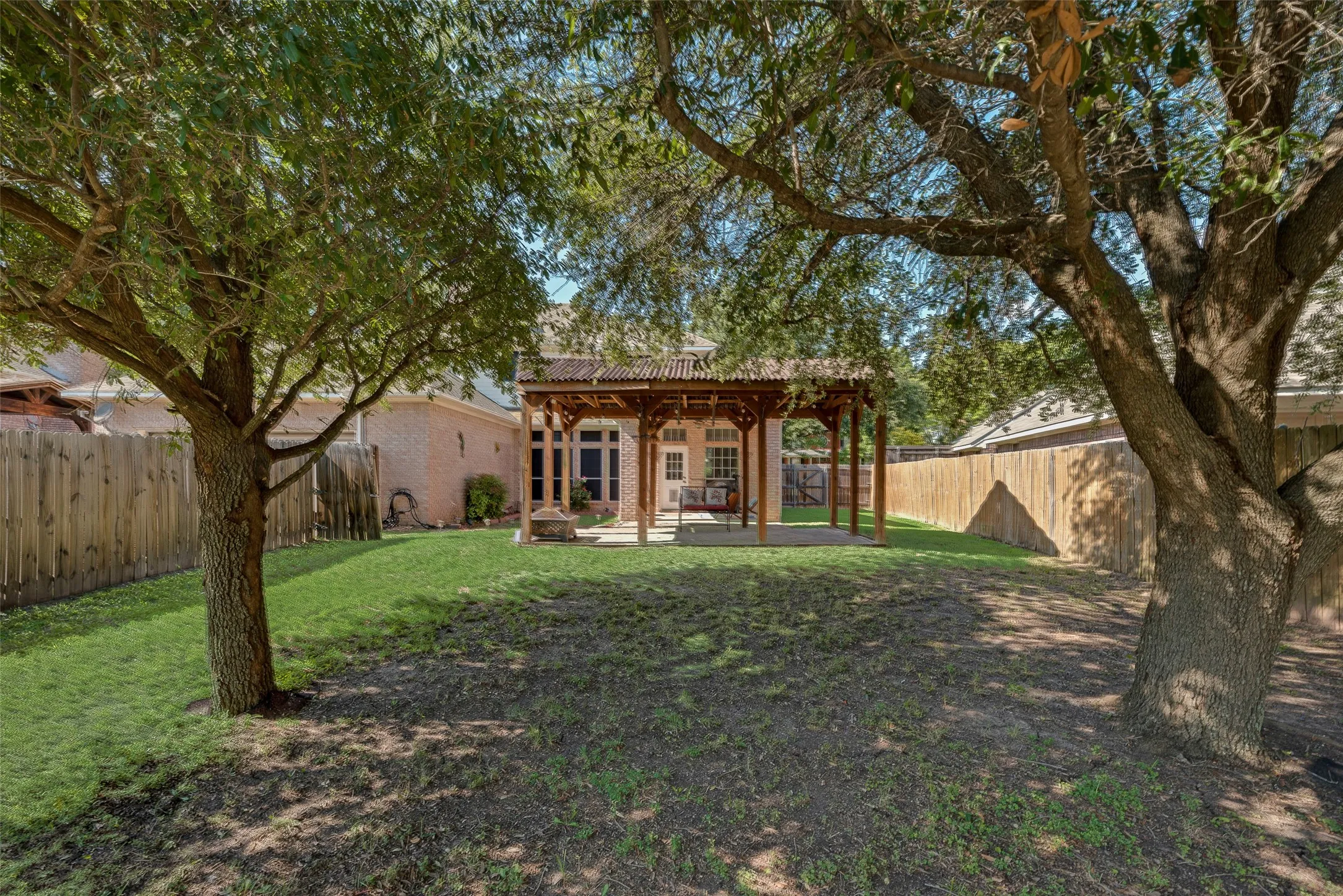 Expansive backyard featuring a manicured lawn, mature trees, and a covered pergola