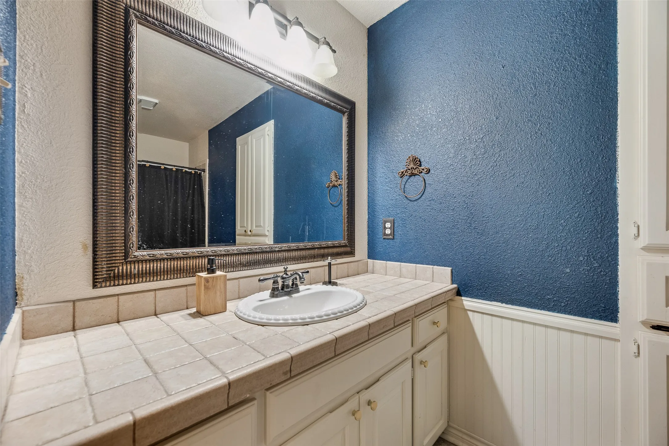 Bathroom vanity with a white ceramic sink, chrome faucet, and tiled countertop