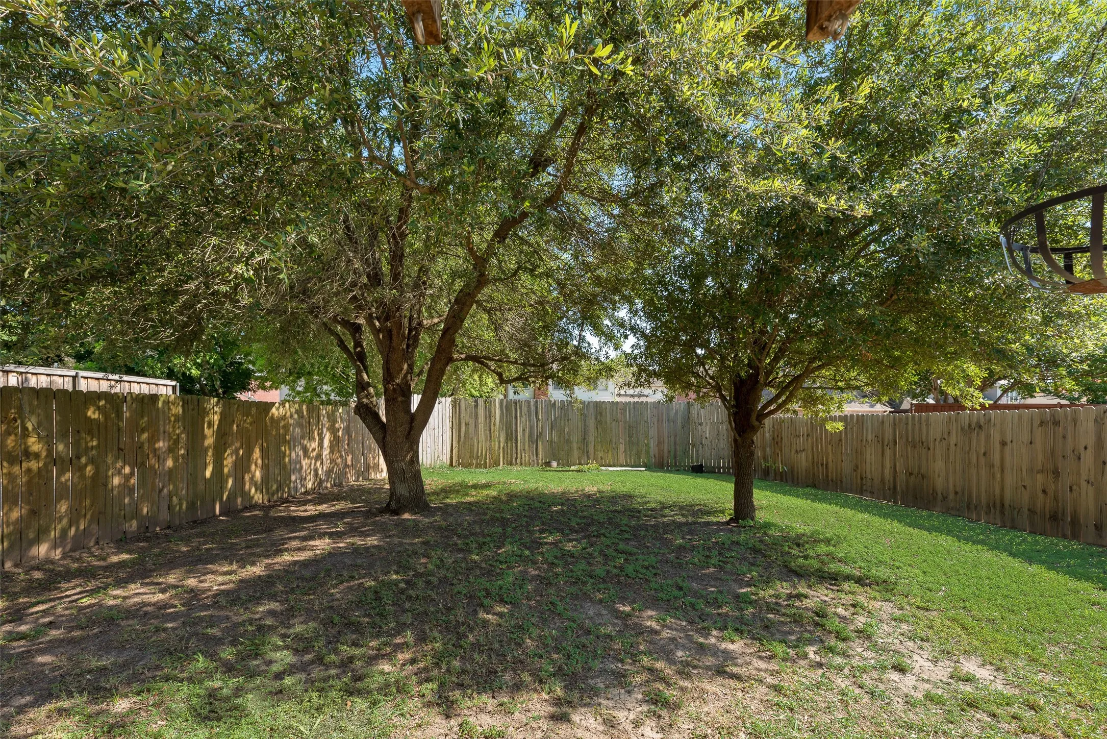 Spacious backyard featuring two mature trees, a wooden privacy fence, and a combination of grass and natural ground cover