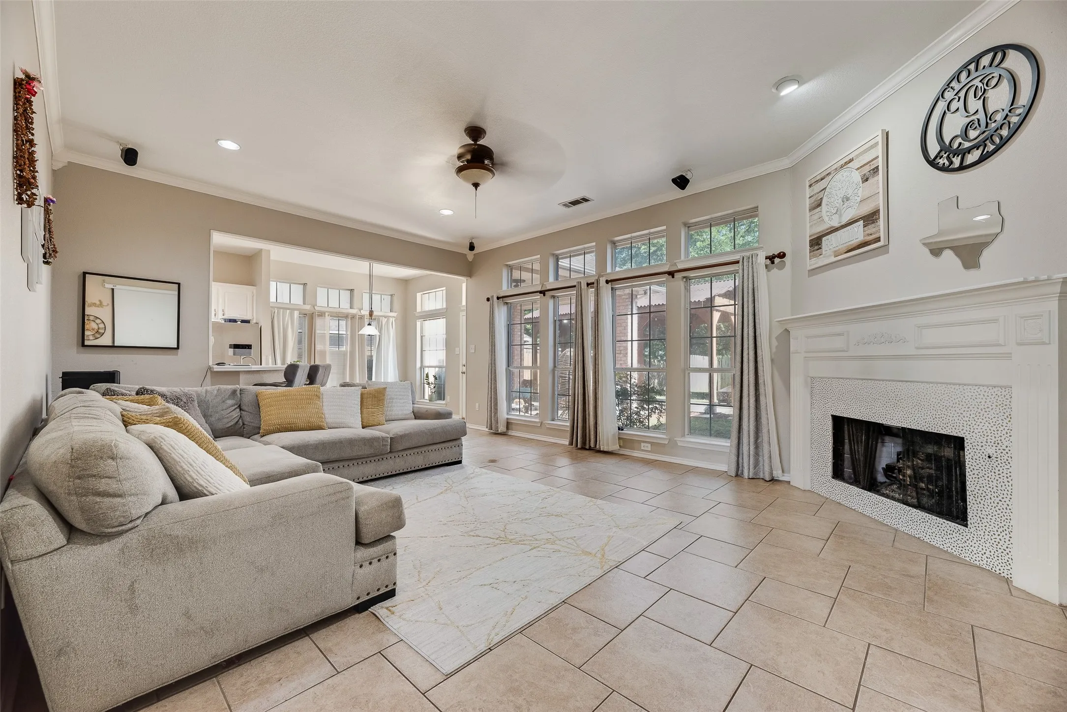 Spacious living area featuring tile flooring, a detailed white mantelpiece, a fireplace with a mosaic tile surround, recessed lighting, and multiple windows with transoms