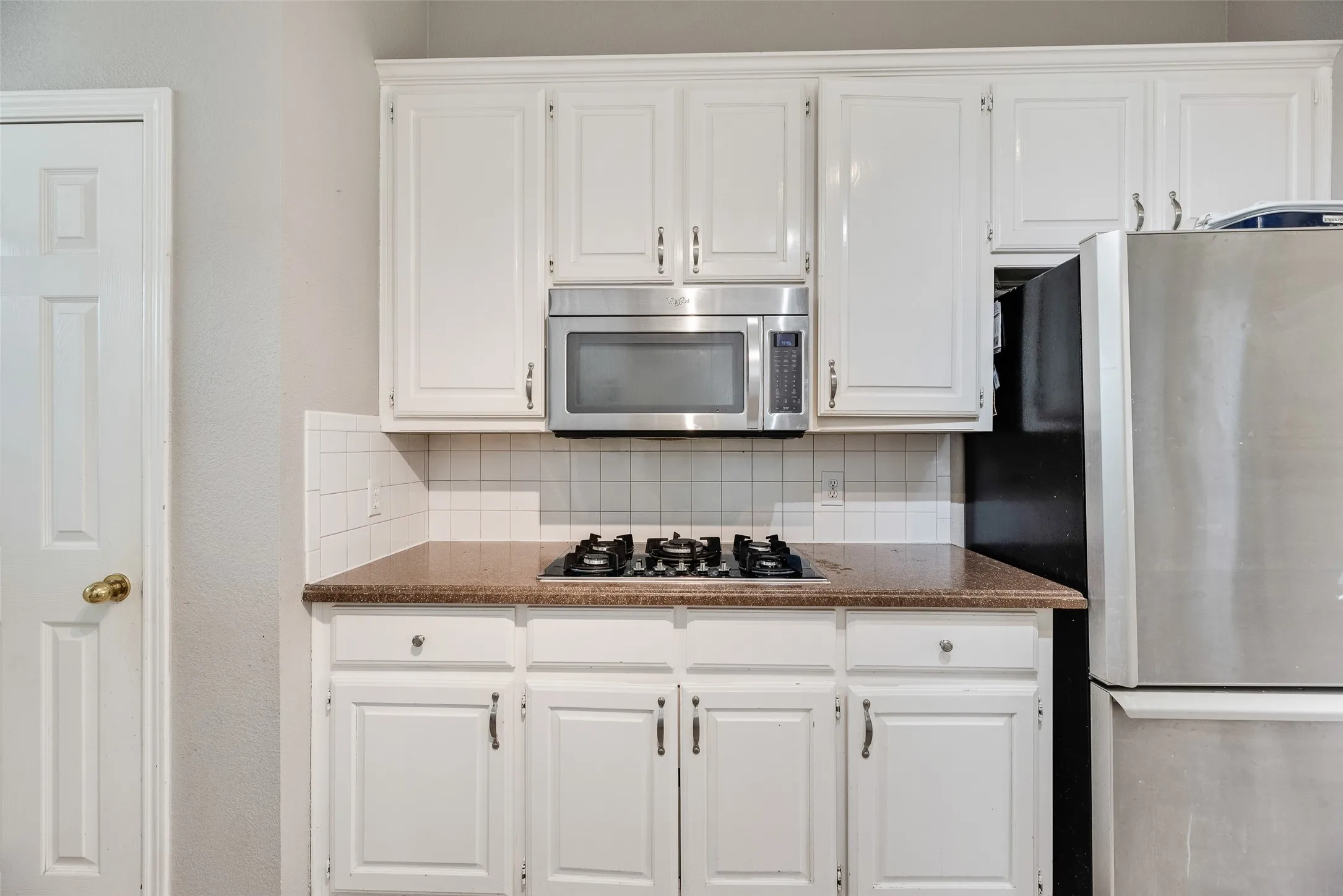 Kitchen featuring white cabinetry, a built-in microwave, a gas cooktop, and a stainless steel refrigerator