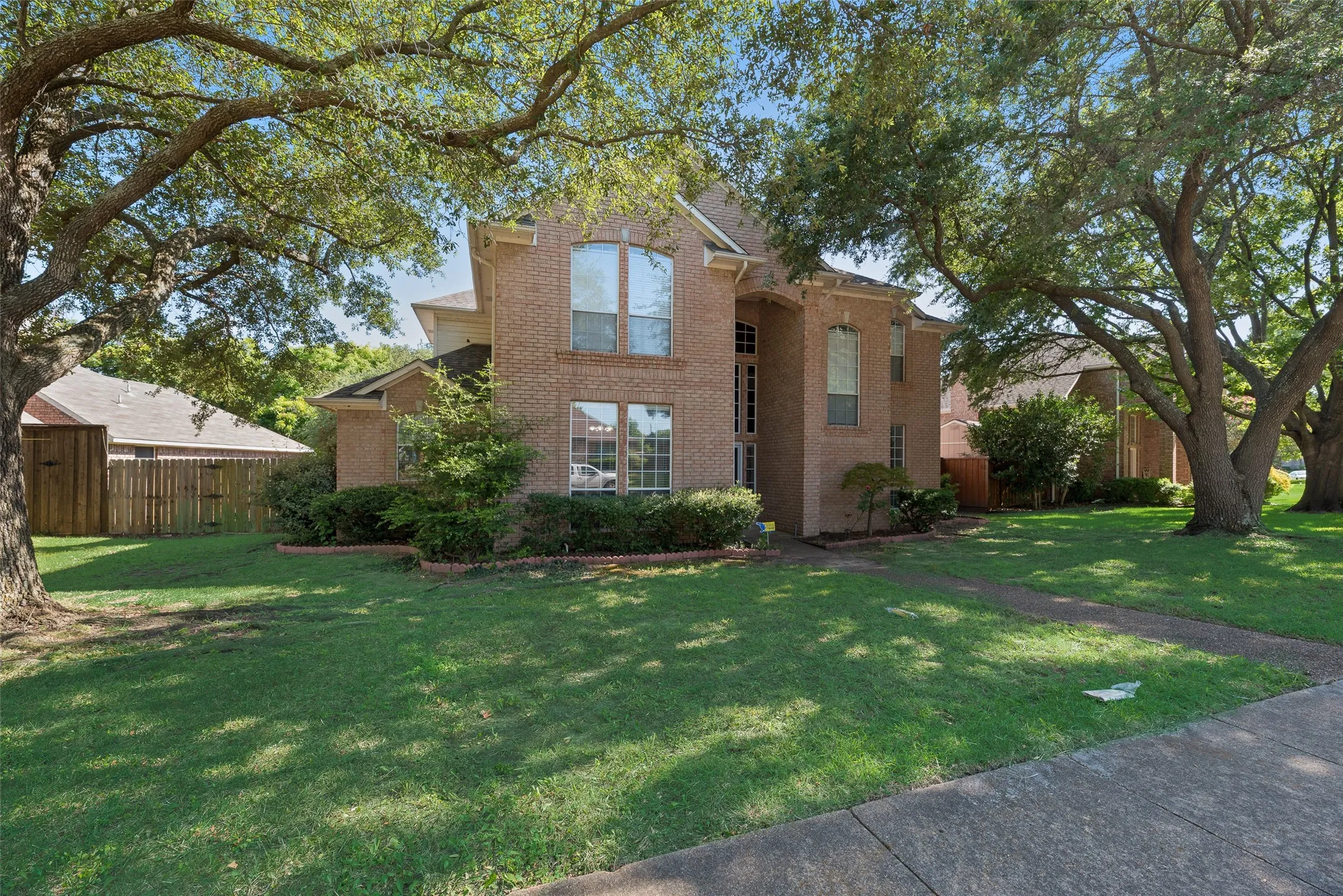 Two-story brick exterior featuring multiple arched windows, mature trees, and a concrete sidewalk