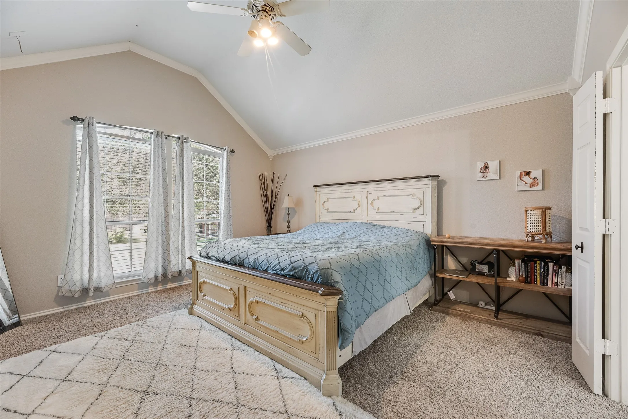 Vaulted ceiling with crown molding, ceiling fan, carpet flooring, and three paned windows with blinds