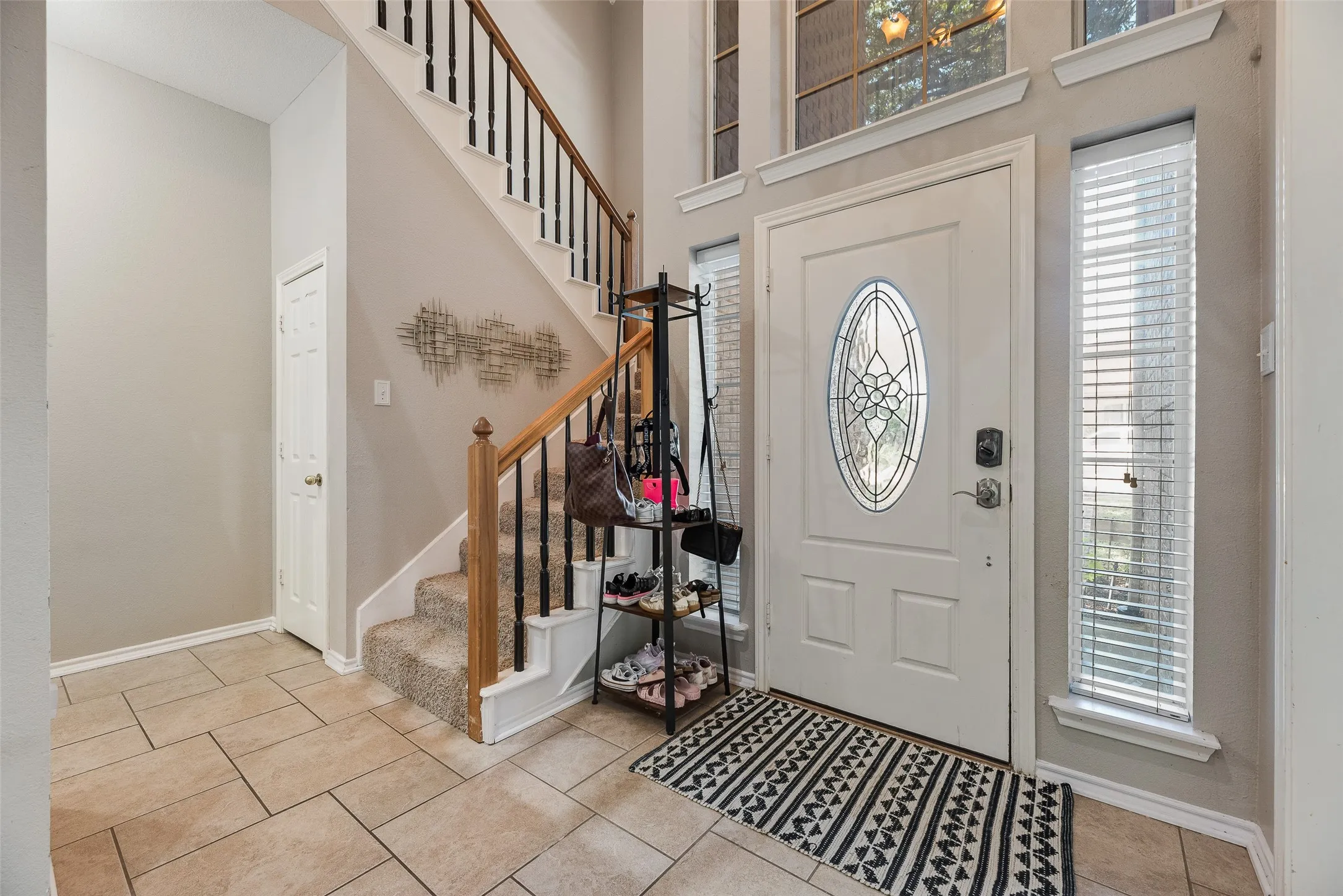 Foyer featuring tile flooring, a two-story ceiling, a staircase with wood handrails and black balusters, and a front entry door with an oval leaded glass insert and transom windows