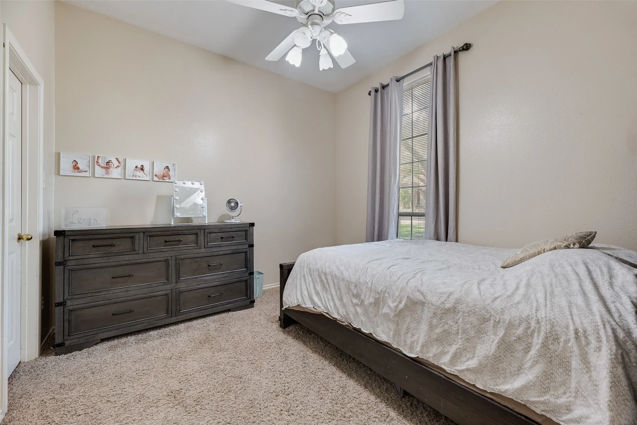 Room featuring a vaulted ceiling with a white ceiling fan, carpet flooring, and a large window with gray drapes