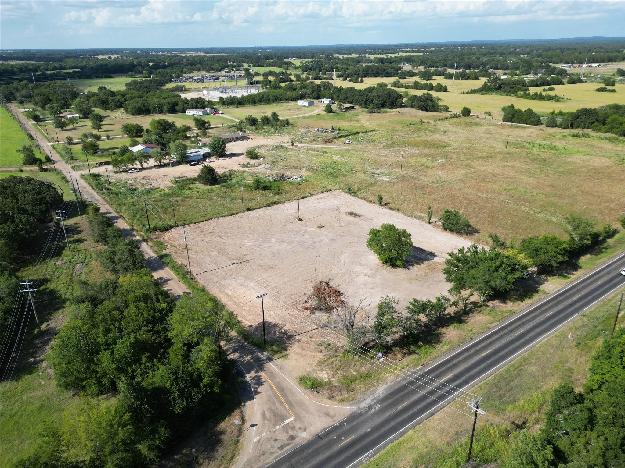 Expansive land parcel featuring direct road frontage, a cleared building area, and mature trees providing natural screening