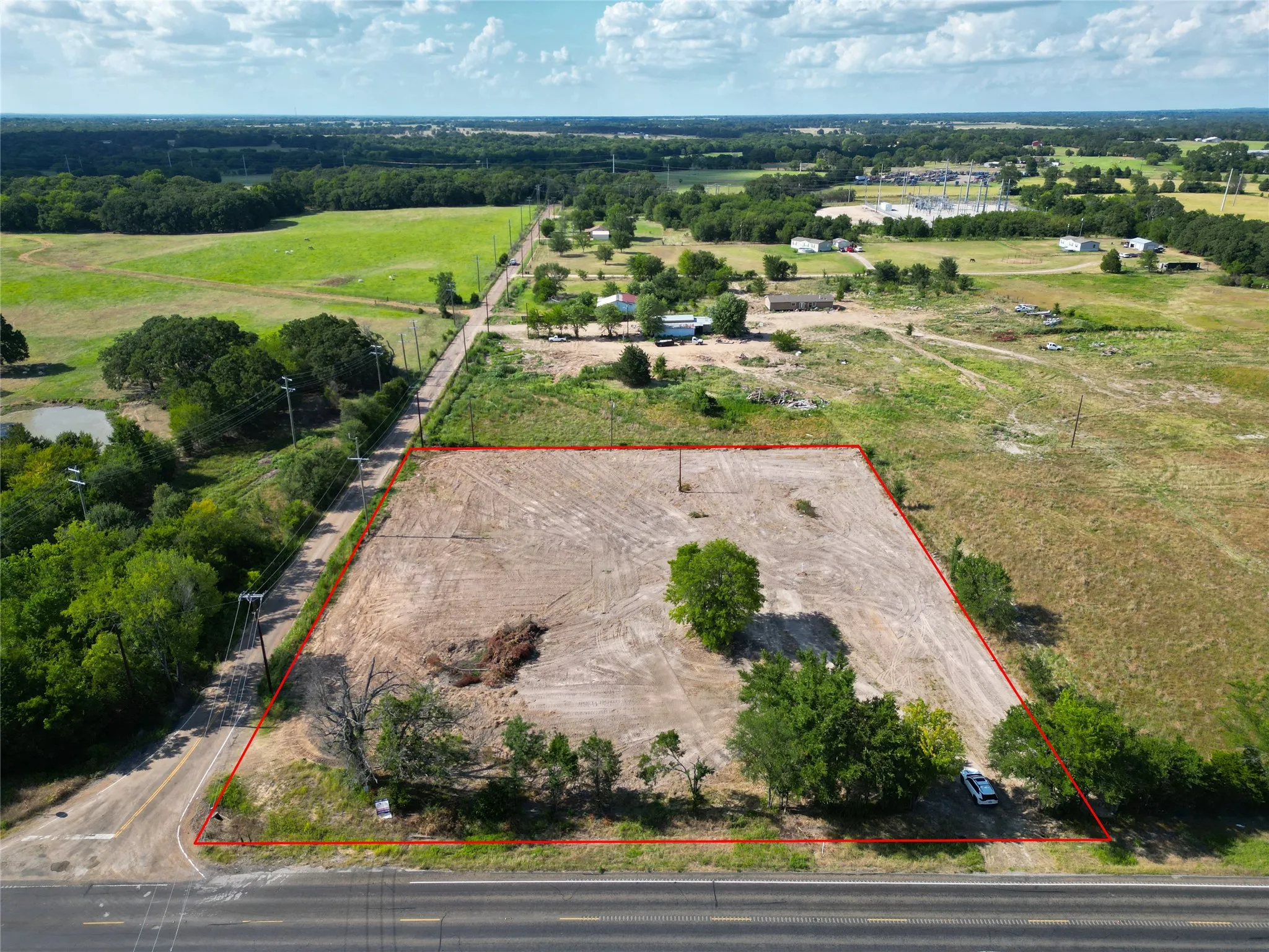 Expansive cleared lot outlined in red, featuring direct road frontage and scattered mature trees