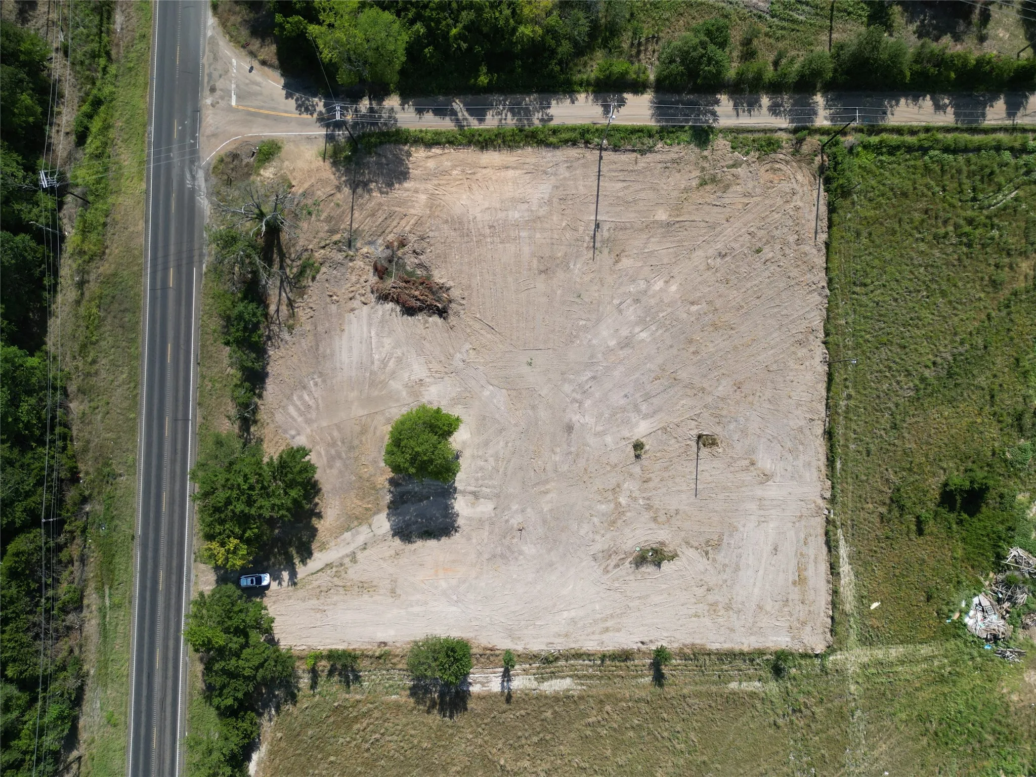 Cleared land parcel featuring an established perimeter, adjacent road frontage, and remaining mature trees