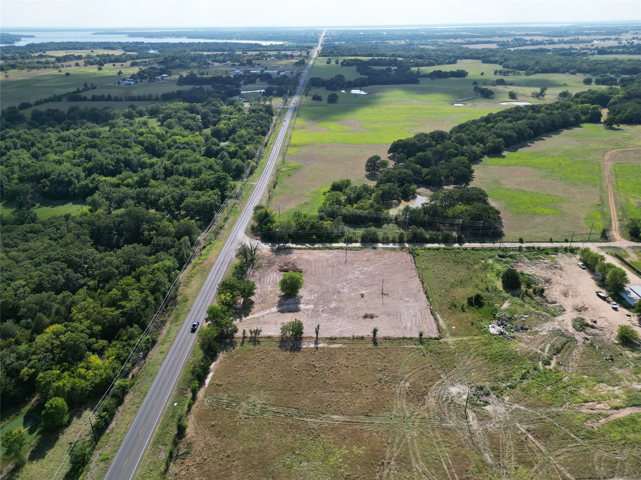 Expansive property featuring cleared land, surrounding wooded areas, and a paved road frontage