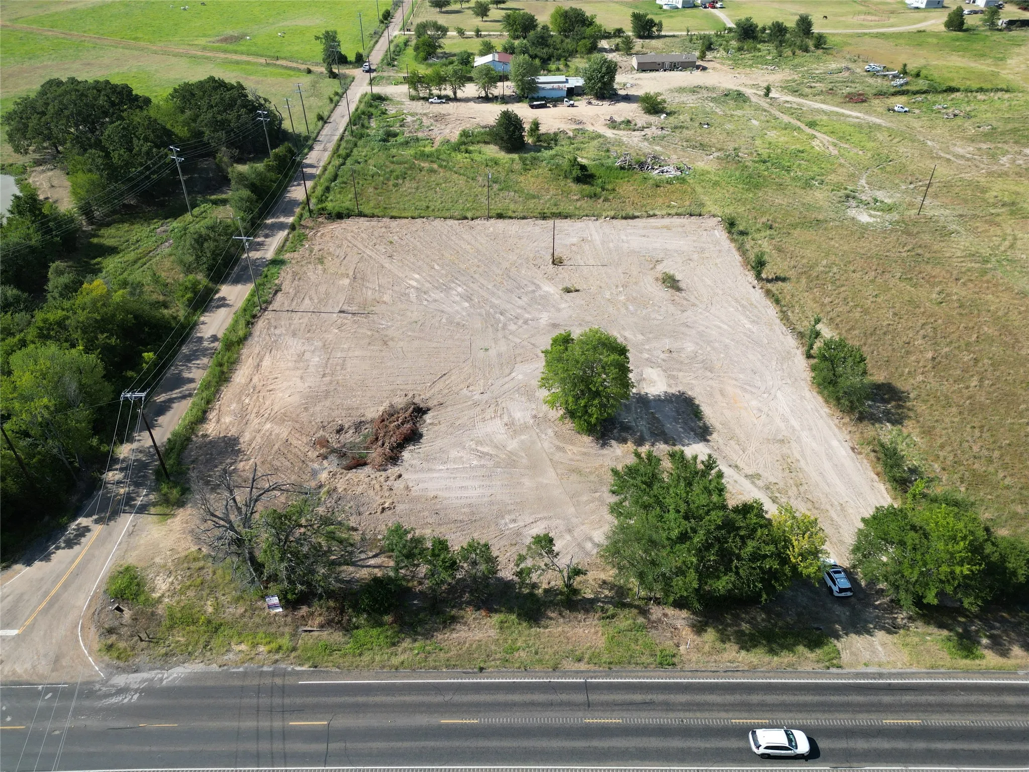Expansive land parcel featuring cleared ground, mature trees, and direct road frontage