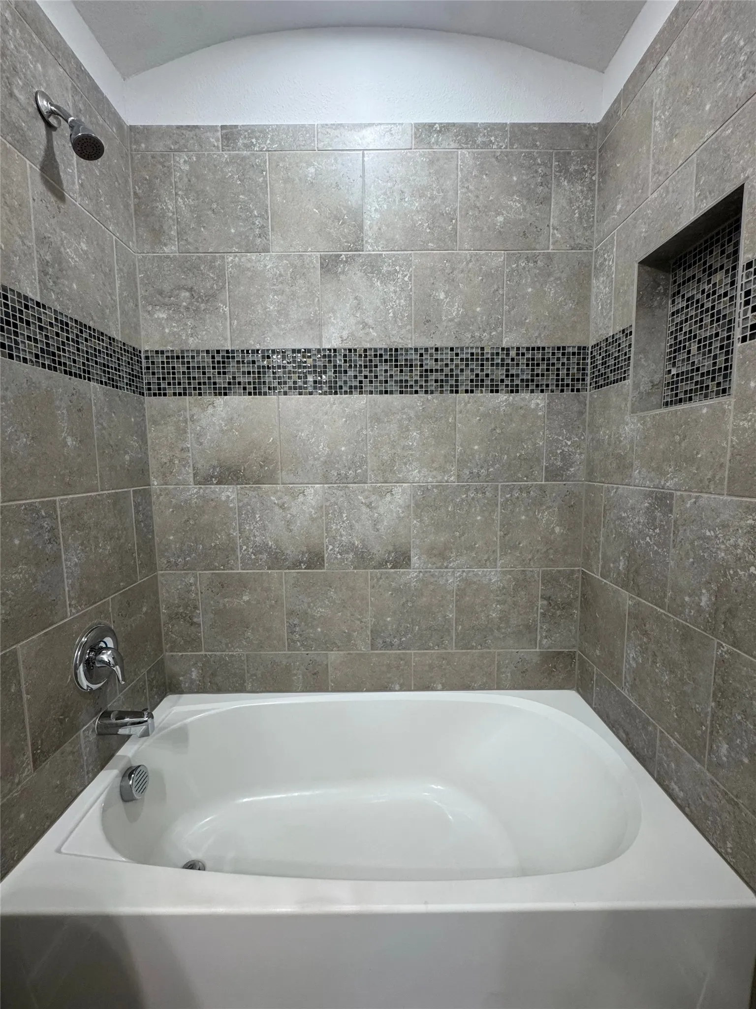 Bathtub with tiled surround, mosaic accent band, and integrated shower niche