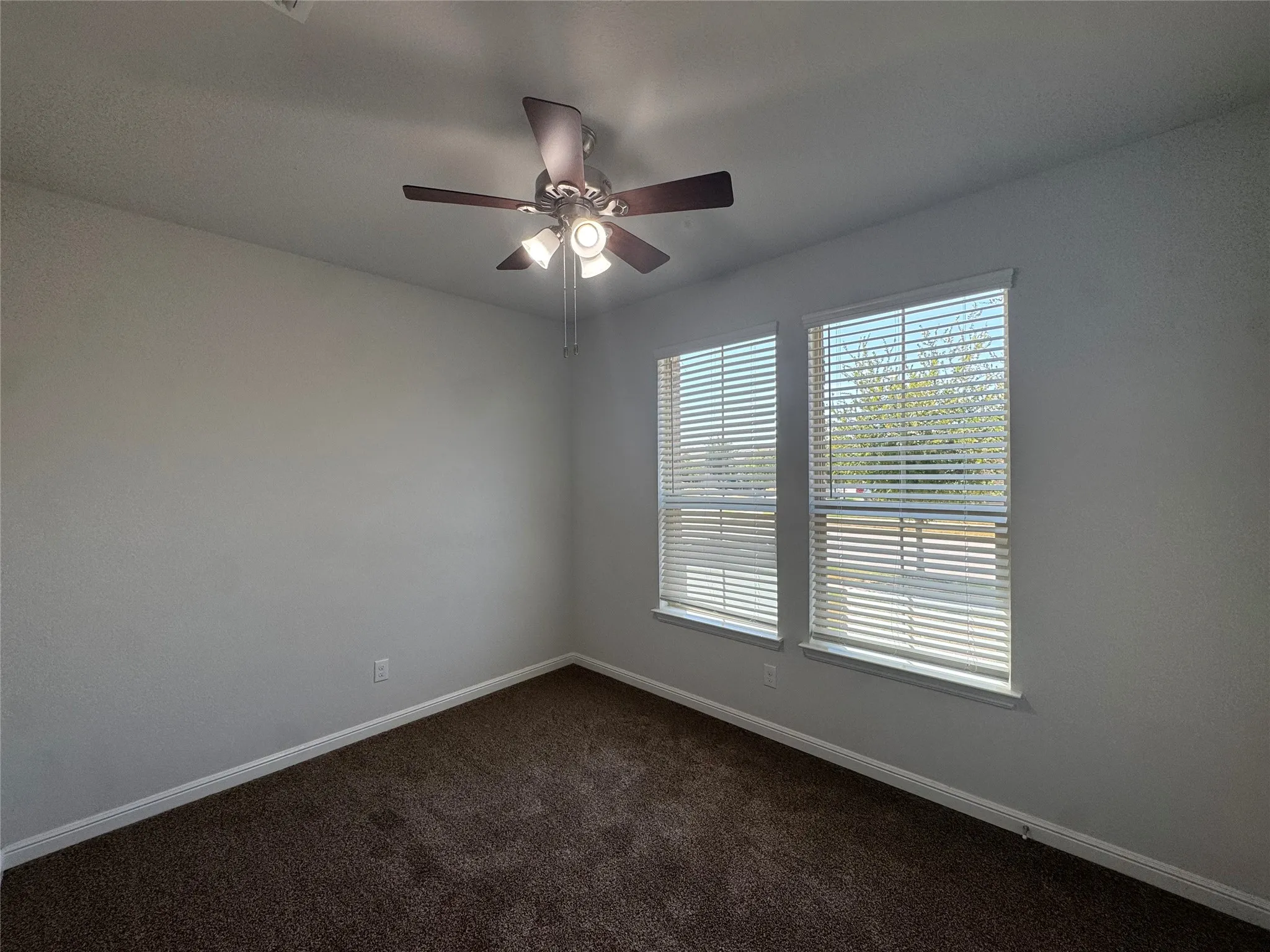 Two windows with horizontal blinds, overhead ceiling fan with integrated lighting, and textured wall finish