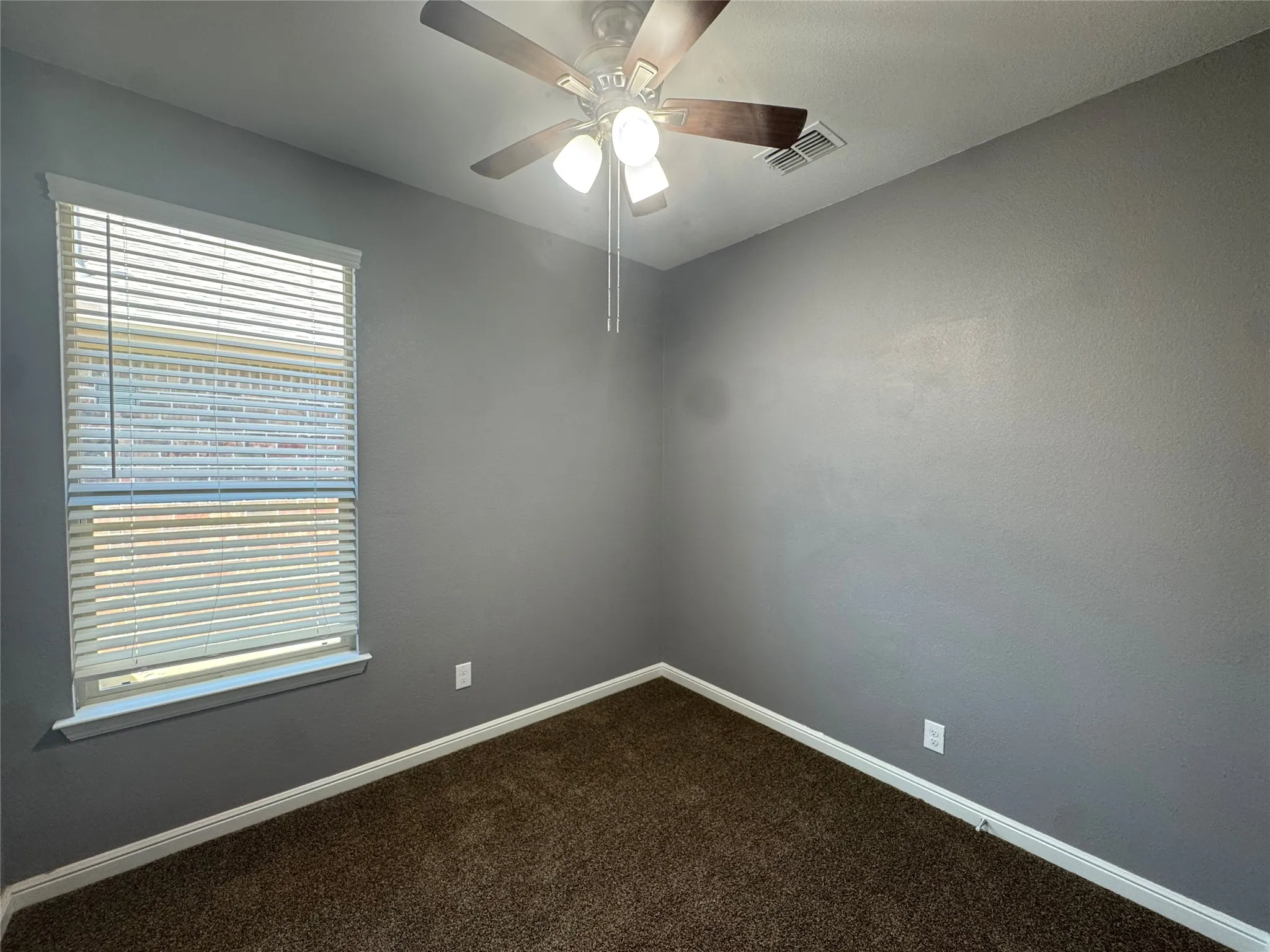 Neutral wall finish, ceiling fan with integrated lighting, window with horizontal blinds, and brown carpet flooring