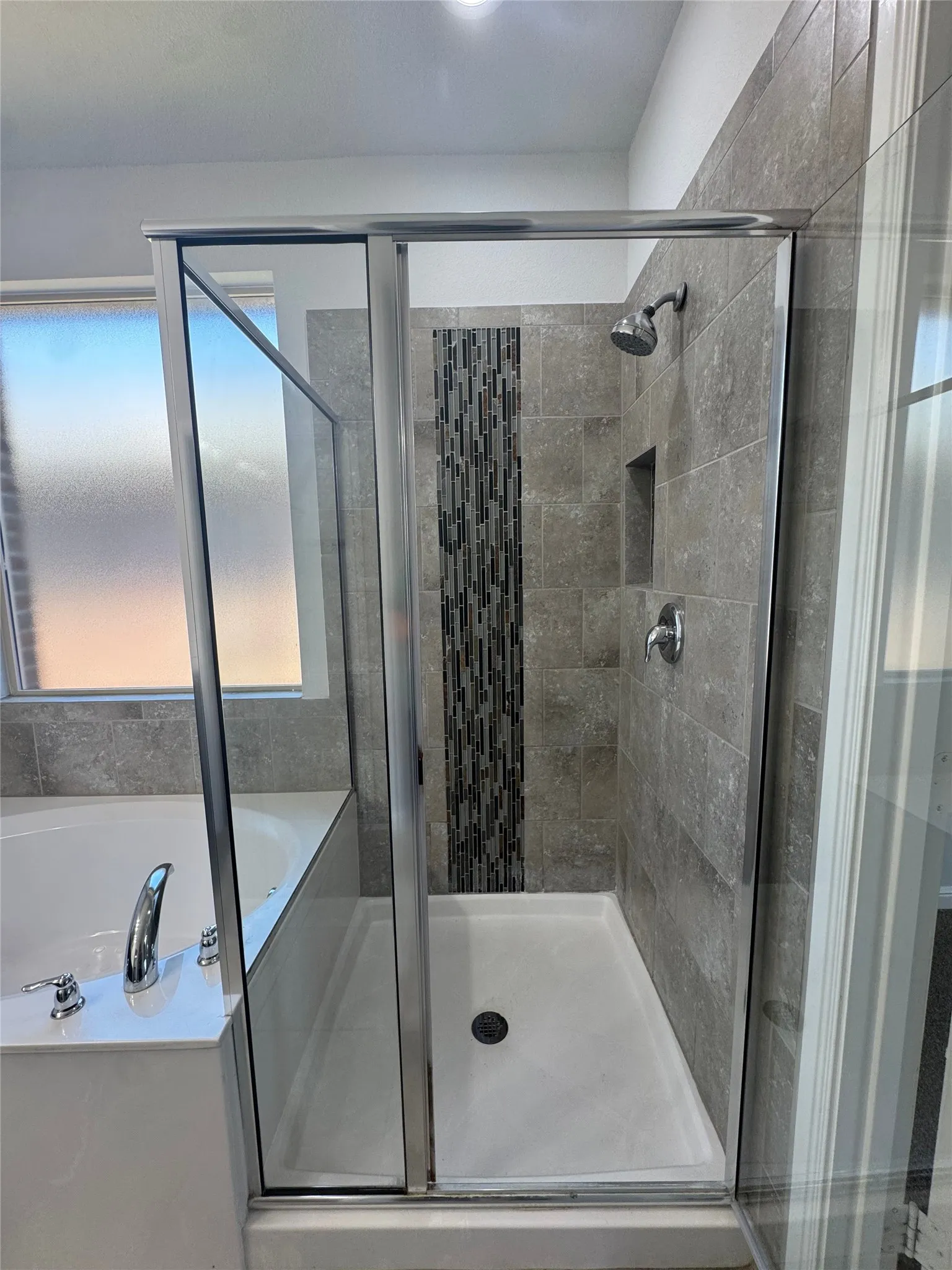 Glass-enclosed shower with gray tiled walls, a decorative tile accent strip, and a built-in shower niche