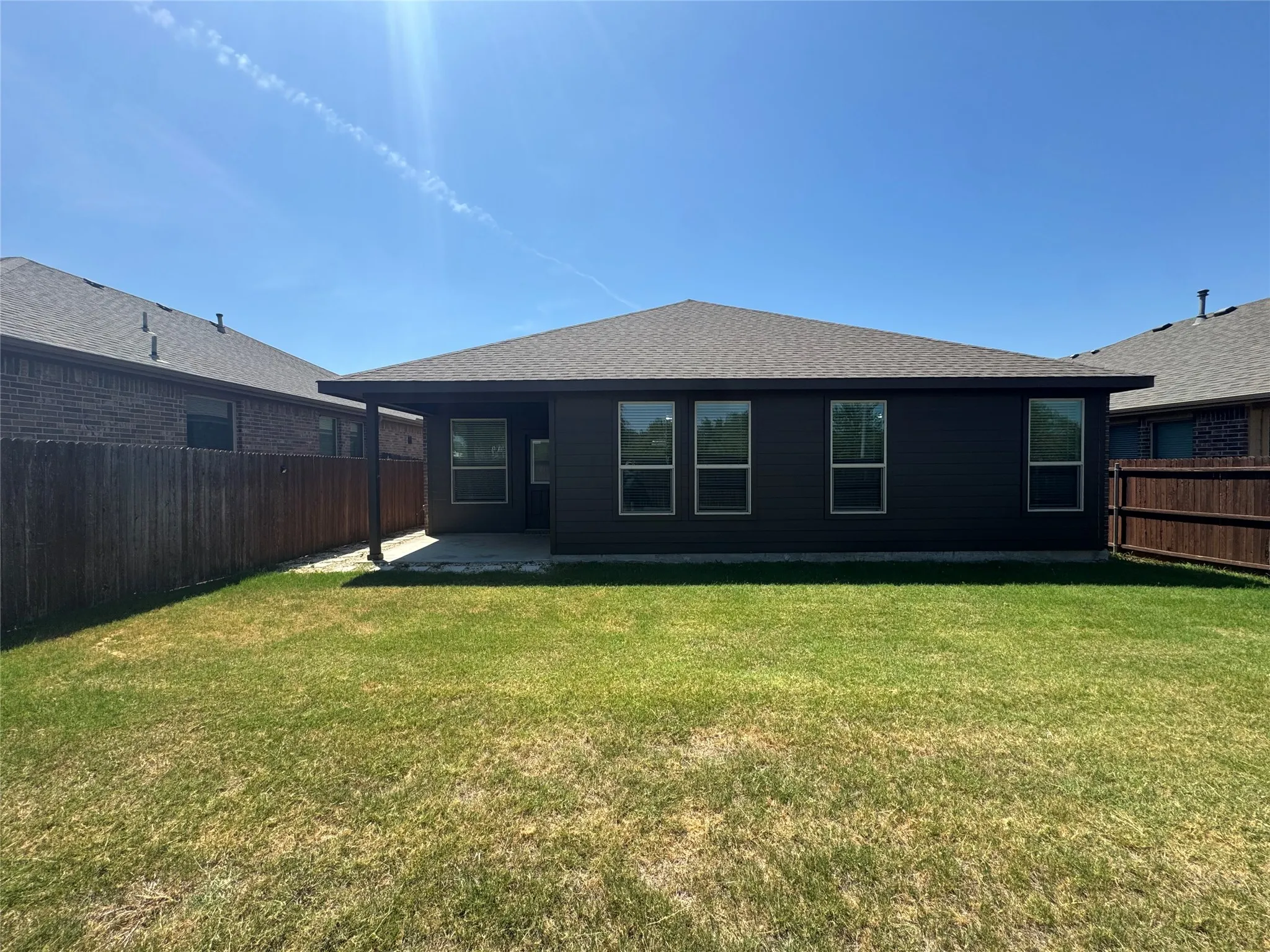 Expansive backyard featuring a manicured lawn, full privacy fencing, and a covered patio with direct outdoor access