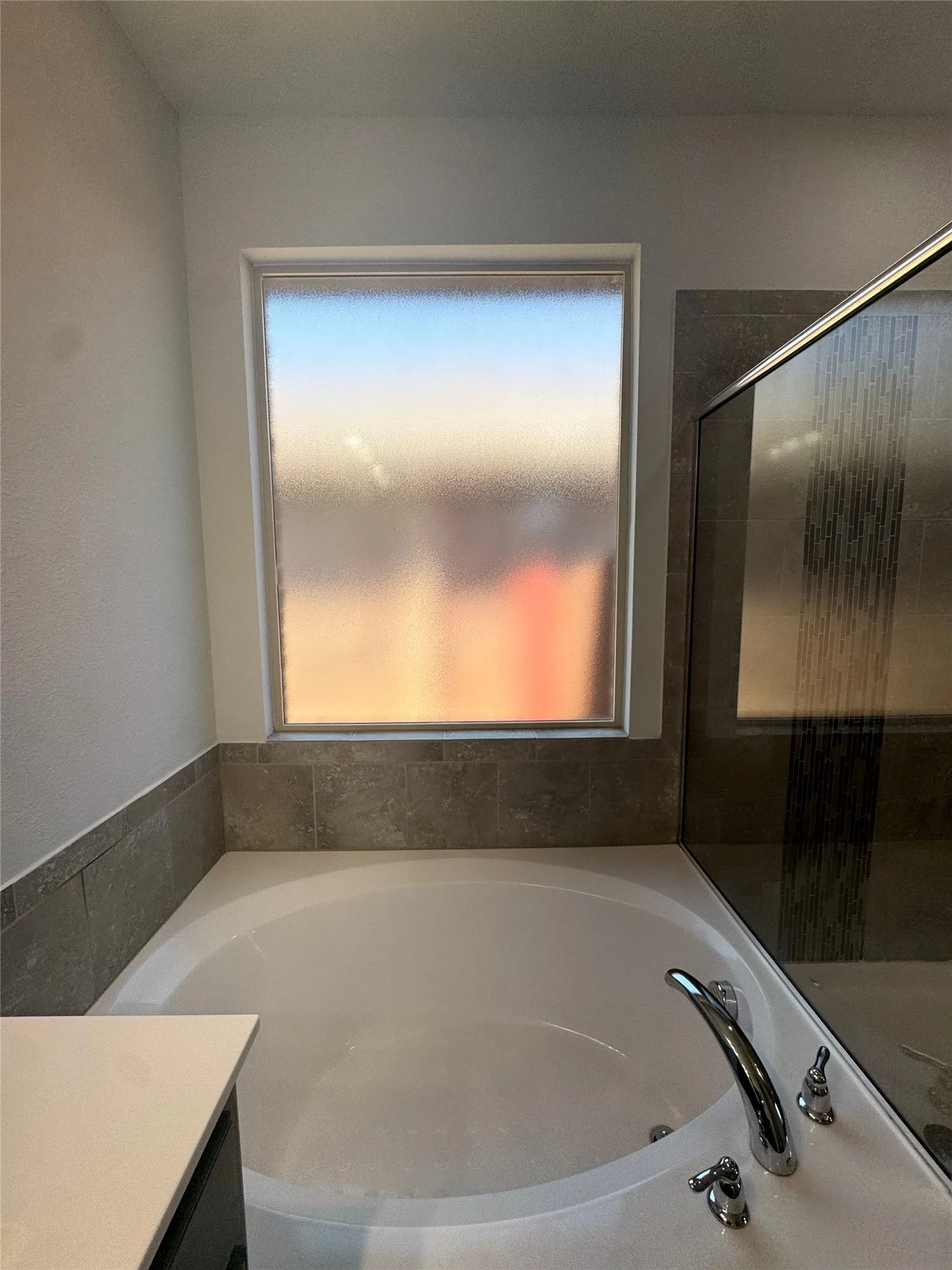 Soaking tub with deck-mounted chrome fixtures, frosted privacy window, and tiled surround